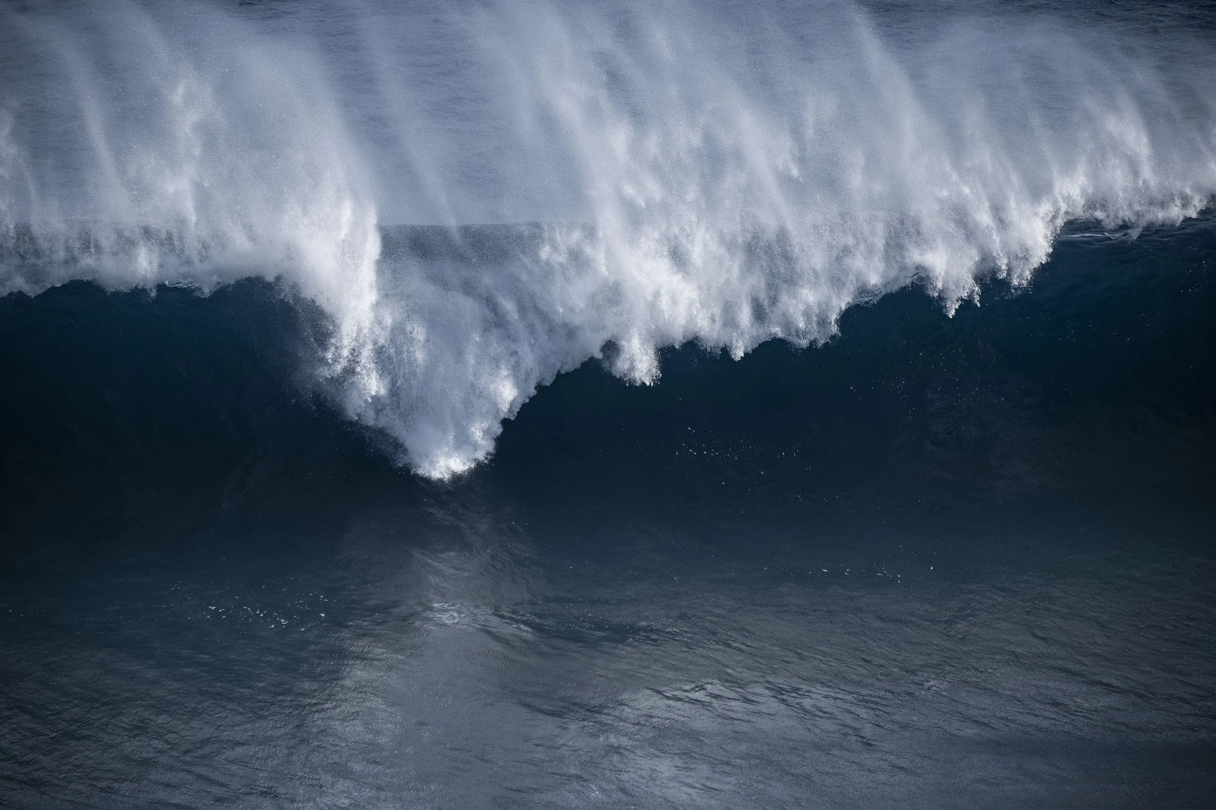 A large ocean wave with white spray at the top, in deep blue water, in cabo, mexico.