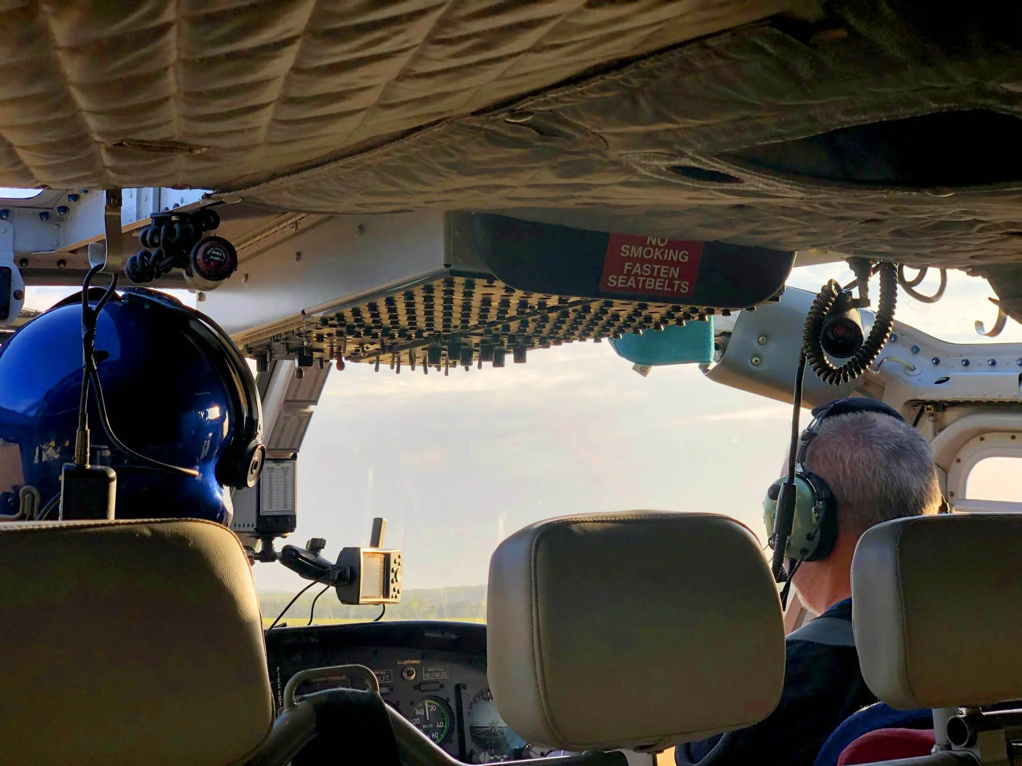 Inside the cockpit of a small airplane with pilots wearing headsets, looking out at a clear sky with trees in the distance. Nighthawks Aviation | Advanced Helicopter Pilot Training