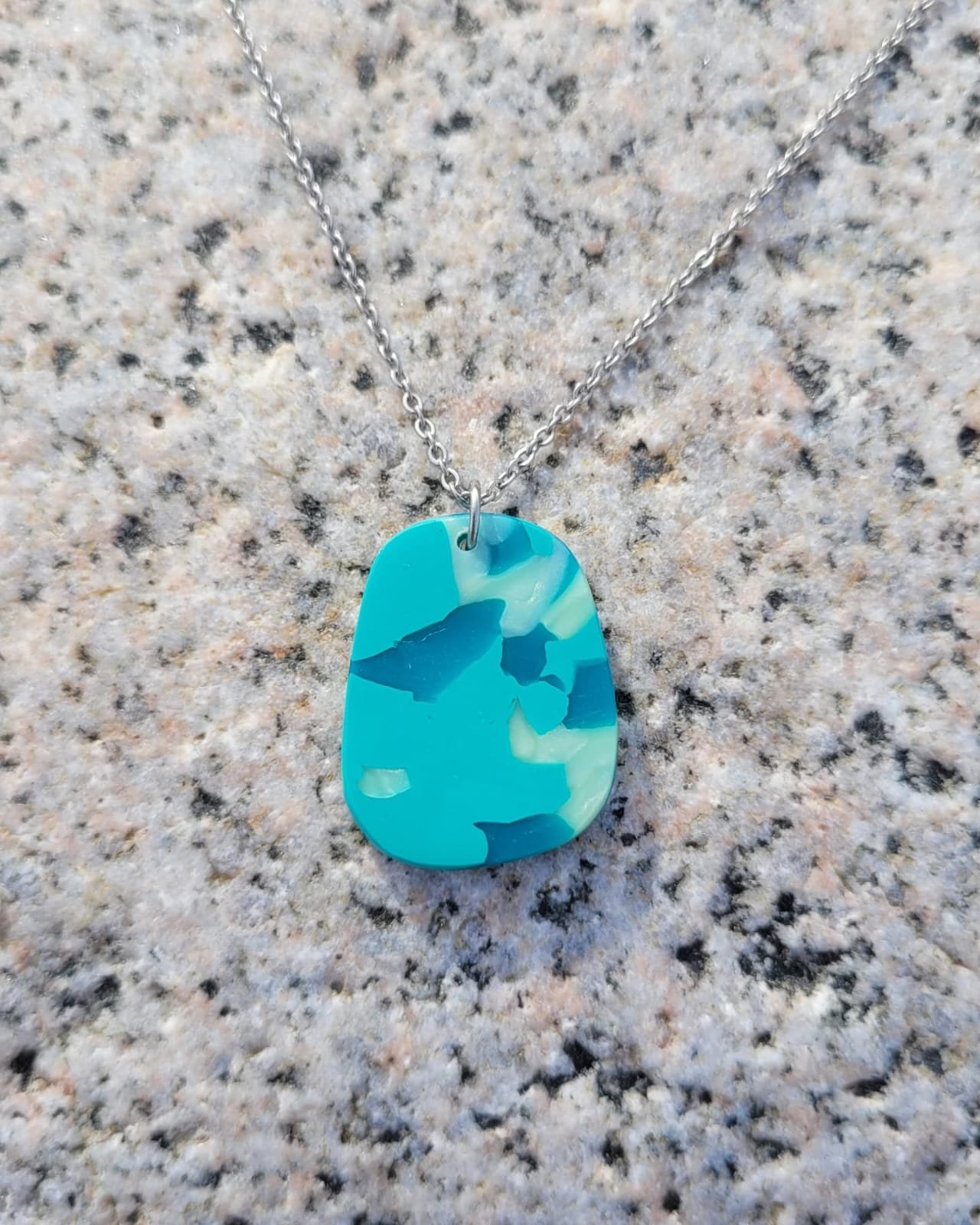 Collar con dijes de piedra en tonos azules, colgado en una cadena de metal, sobre una superficie de granito.