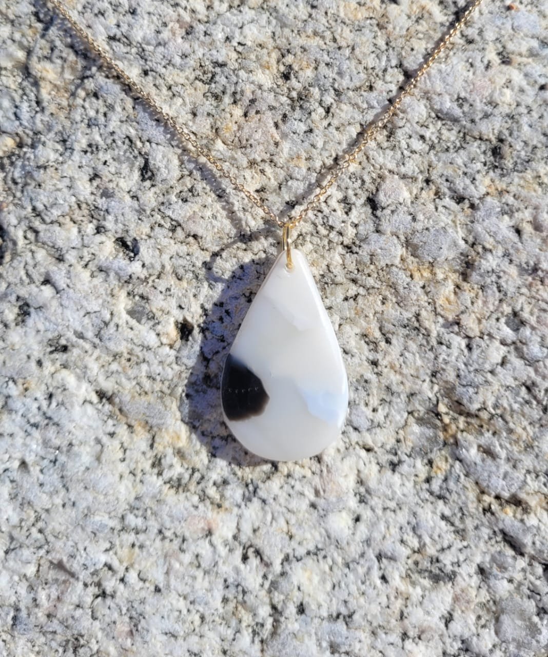Colgante de collar con piedra blanca y negro sobre textura rugosa de color gris