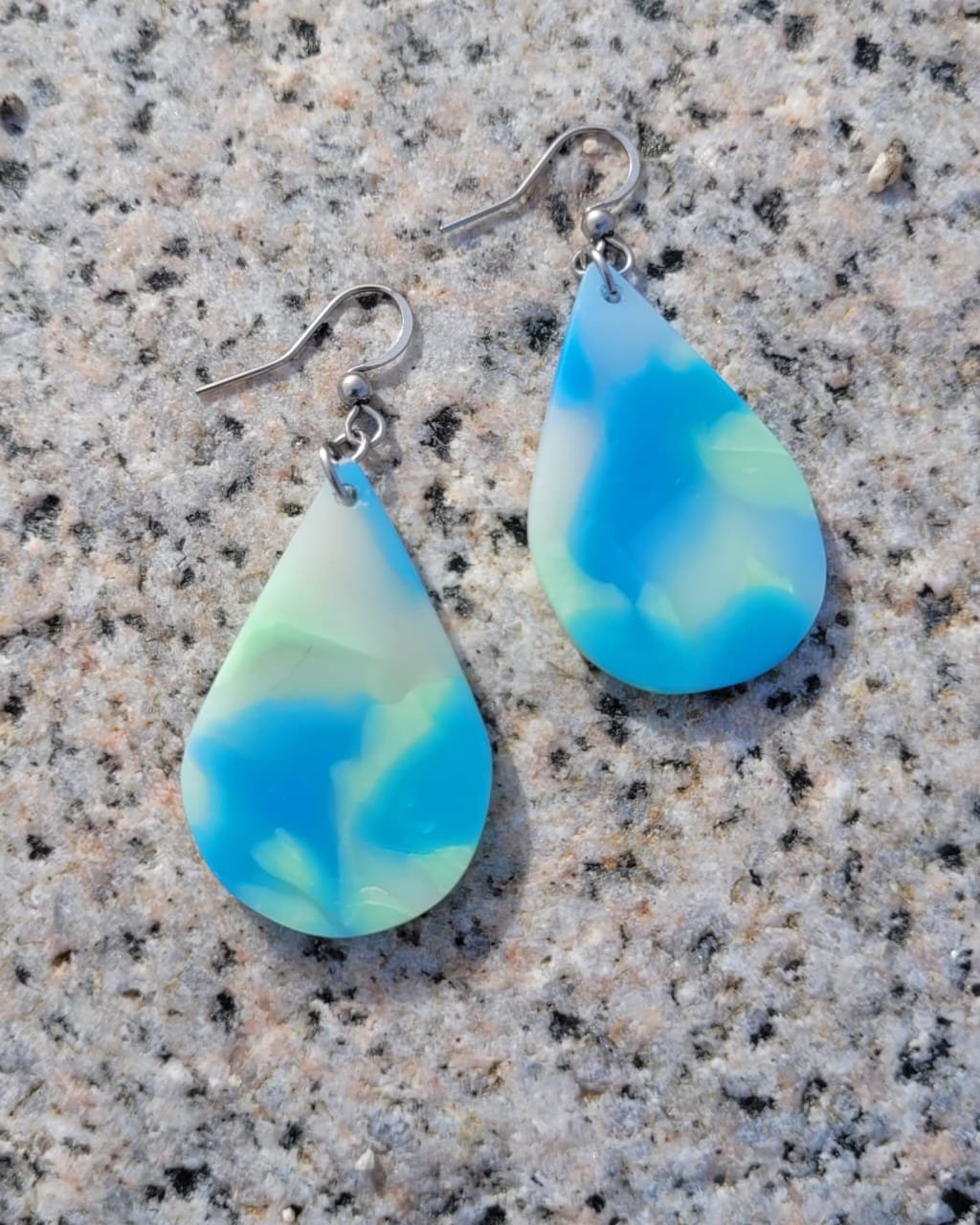 Aretes de plástico en forma de lágrima con tonos azules, verdes y blancos sobre una superficie de granito.