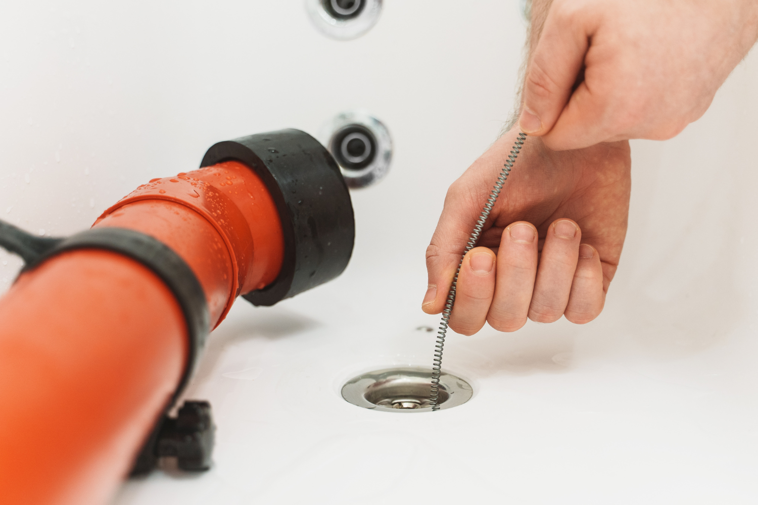 image showing a hand holding a tool used to unclog a drain in a bathtub with hose beside it.