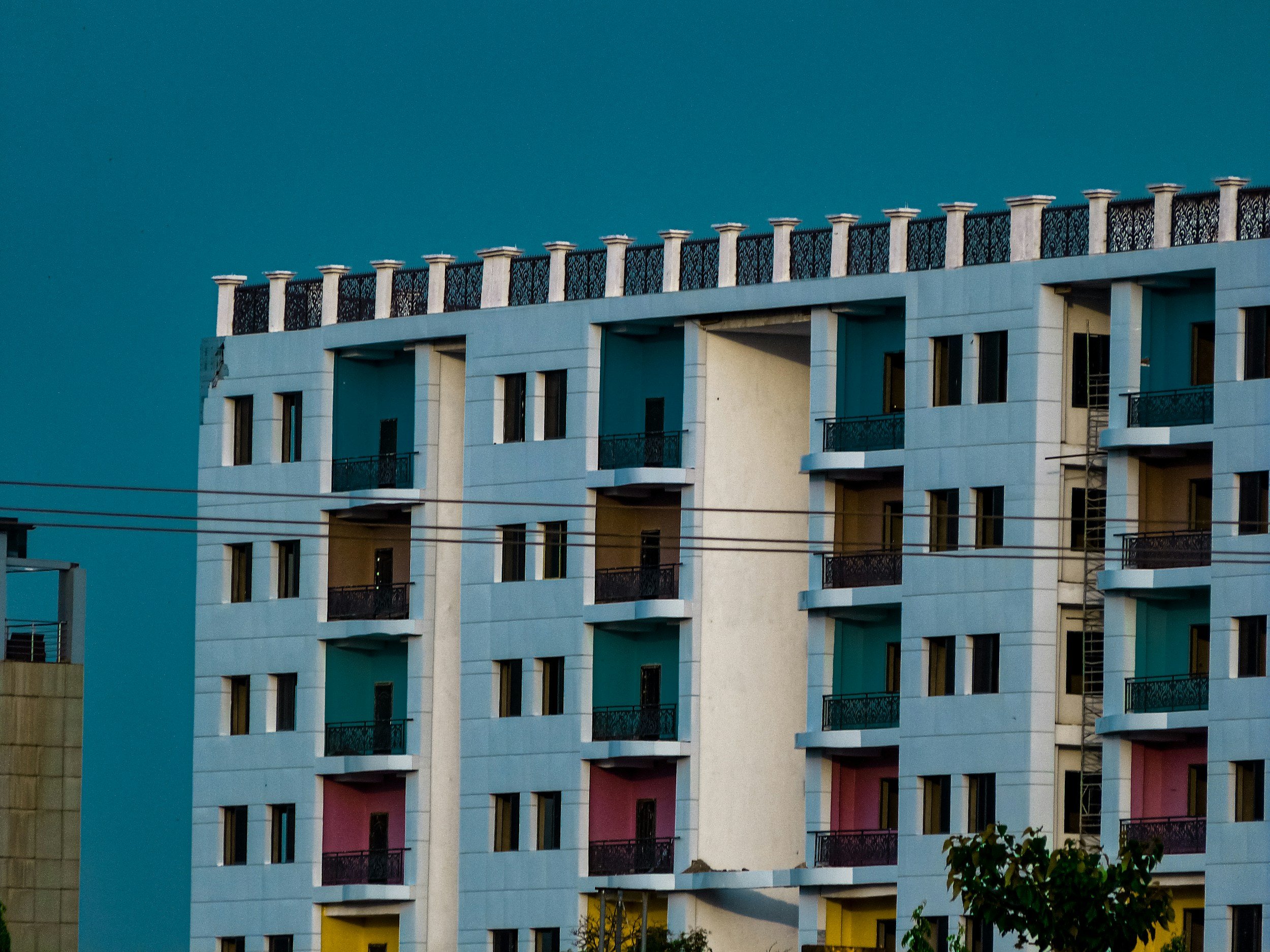 Mehrstöckiges modernes Wohngebäude mit Balkonen in verschiedenen Farben und einem blauen Himmel im Hintergrund.