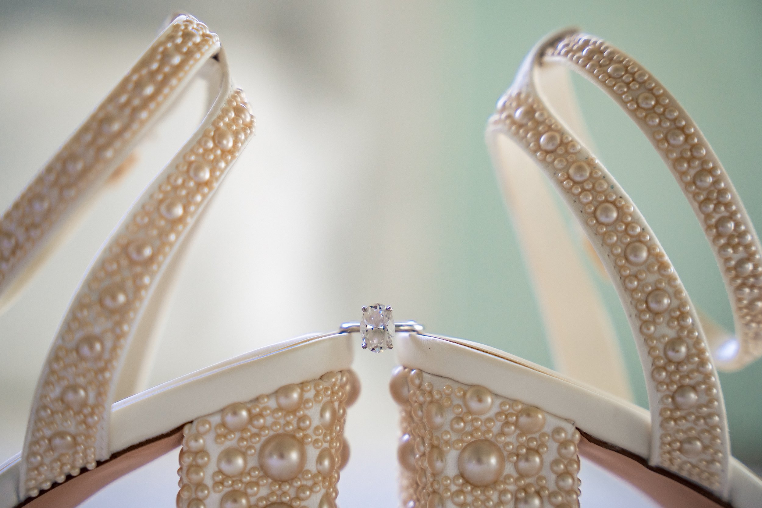 Close-up of a ring with a large central diamond, surrounded by pearl-covered decorative elements that resemble a tiara.
