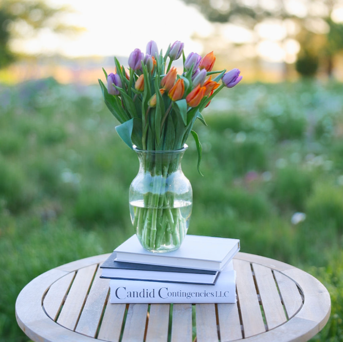 A bouquet of tulips in a clear glass vase sitting on a pile of books on a table outside