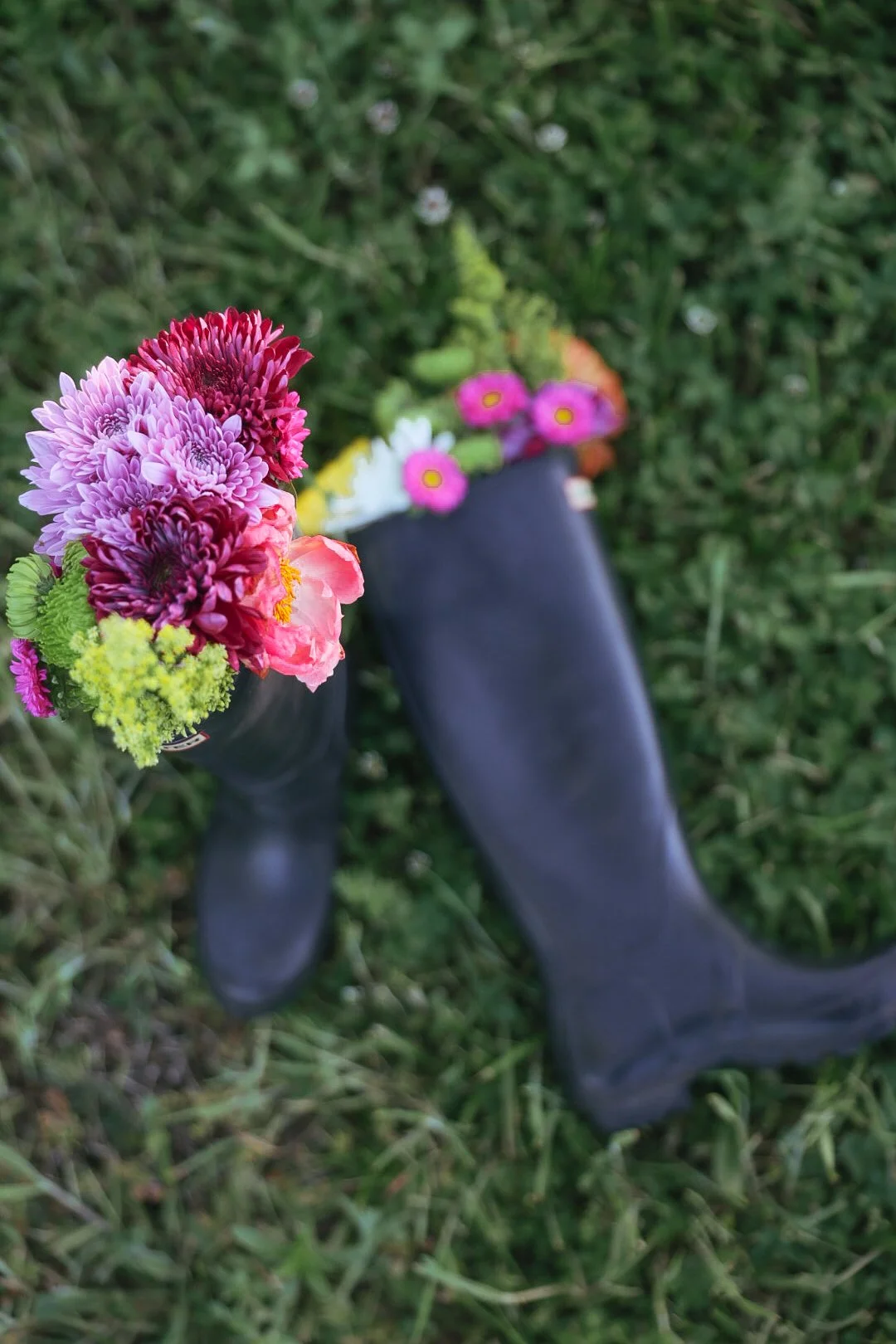 Tall rain boots laying on the grass with flowers sitting inside them
