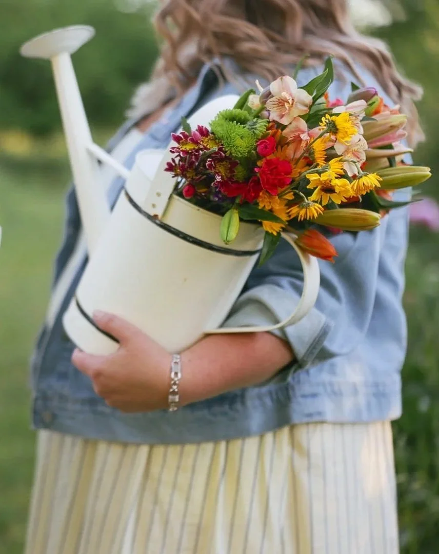 Person holding a watering can filled with colorful flowers.
