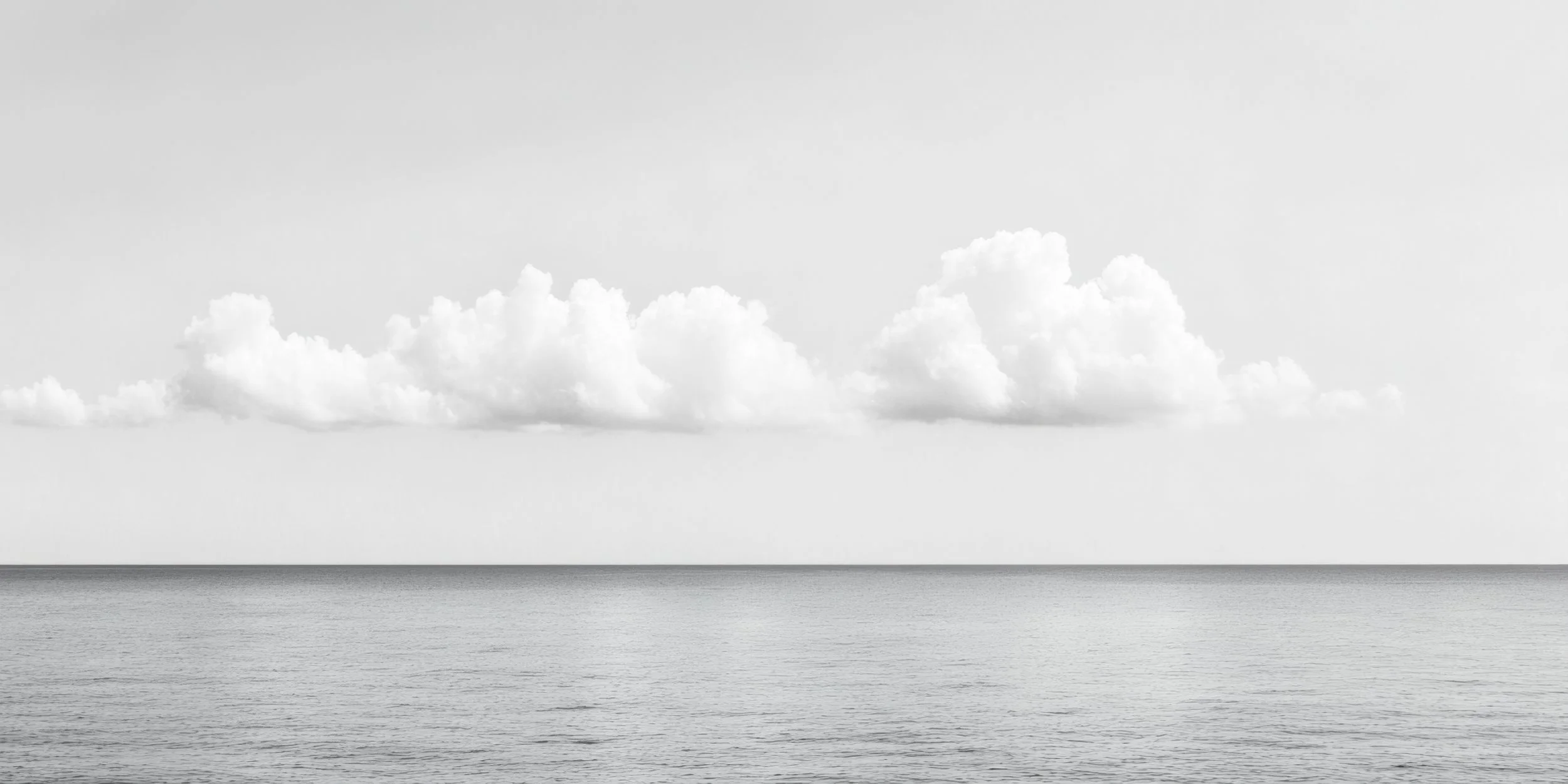 A black and white photograph of a calm sea with a few clouds in the sky.