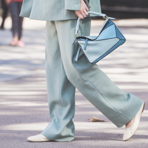 Person in einem Anzug mit einer blauen Tasche, die beim Überqueren einer Straße geht.