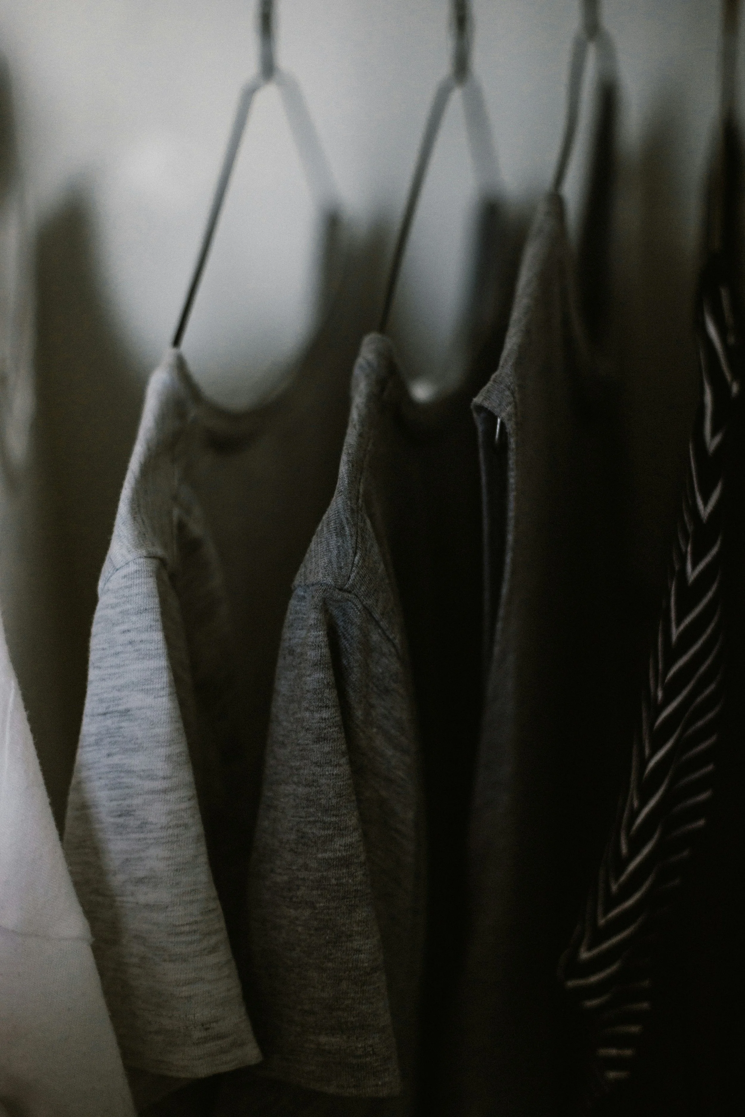 Hanging clothes, including gray shirts and a striped black and white shirt, on a wall hook.