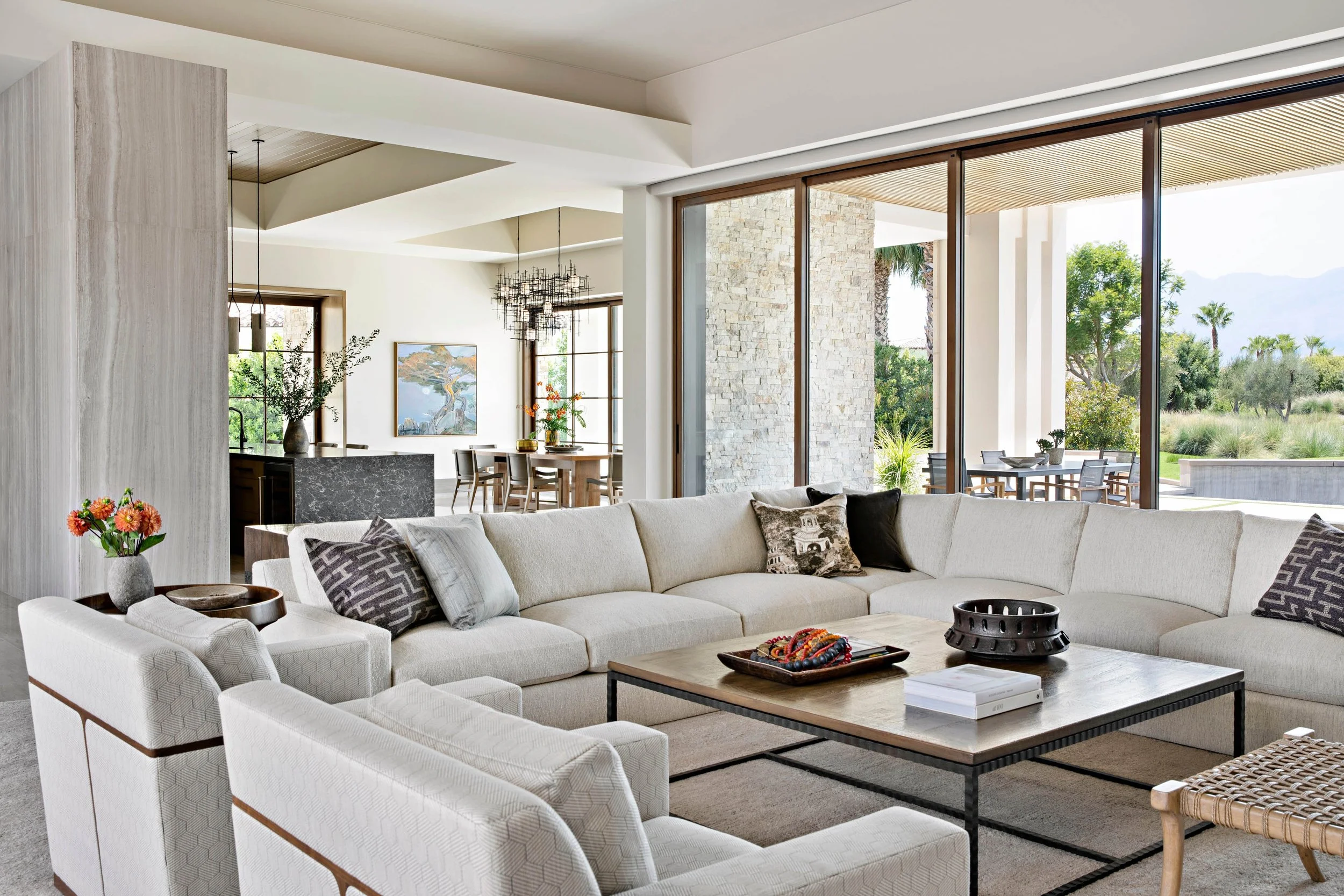 Living room with large beige sectional sofa, coffee table, and view of outdoor patio through large glass doors.