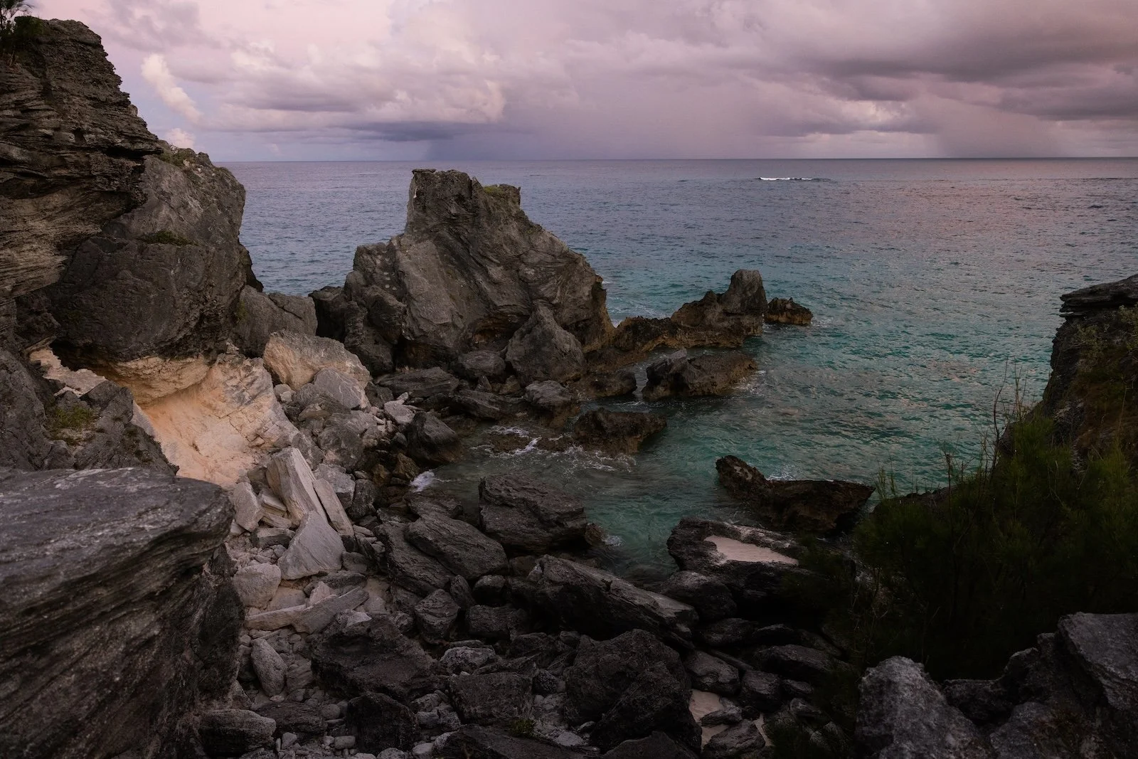 Rocky coastline with large jagged rocks by the ocean under a cloudy sky.