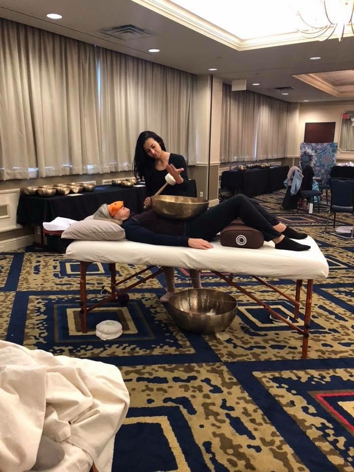 A woman receiving a sound therapy treatment with singing bowls in a hotel conference room.