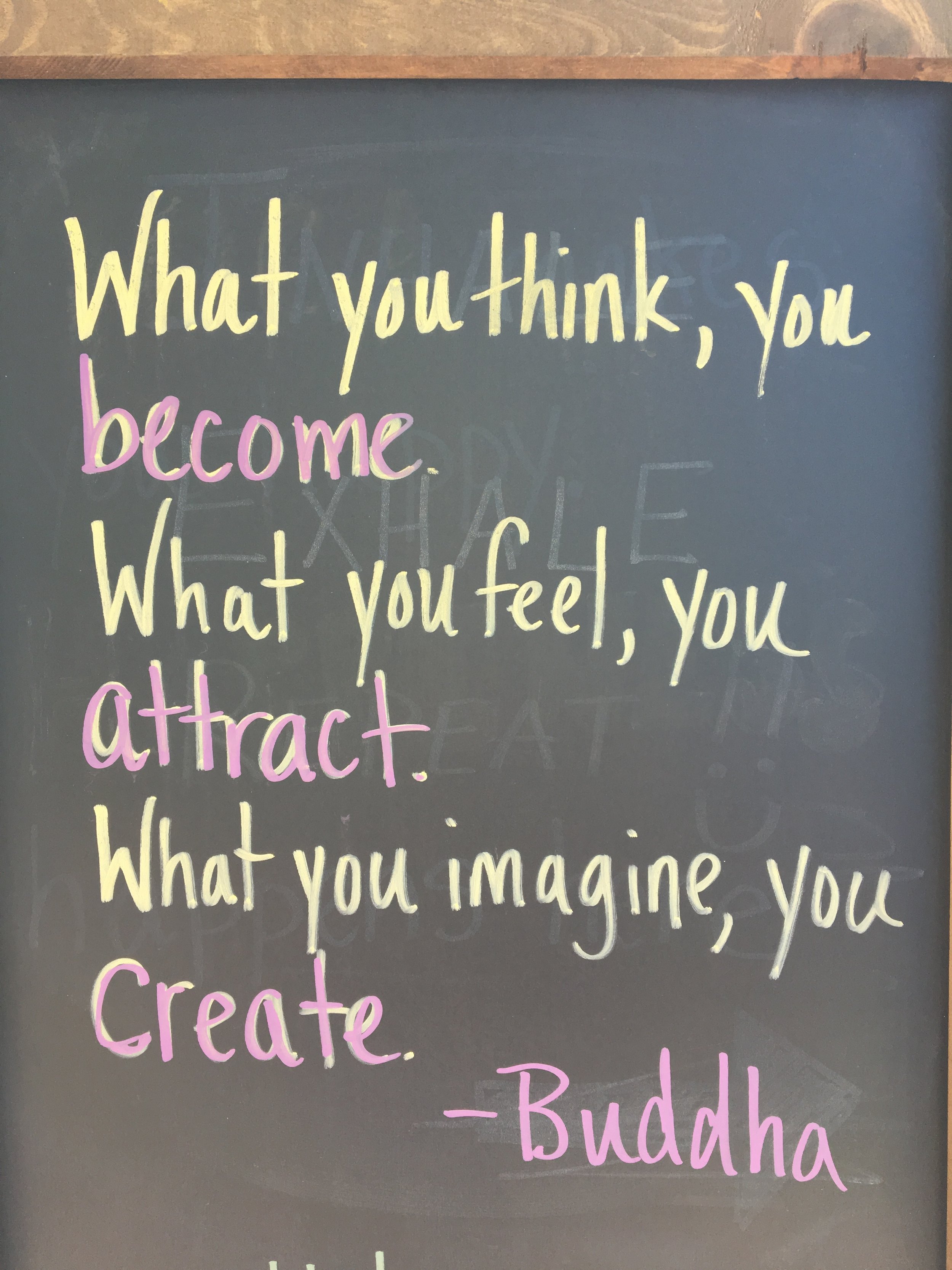 A blackboard with a motivational quote written in yellow, pink, and purple chalk. The quote says, 'What you think, you become. What you feel, you attract. What you imagine, you create.' attributed to Buddha.