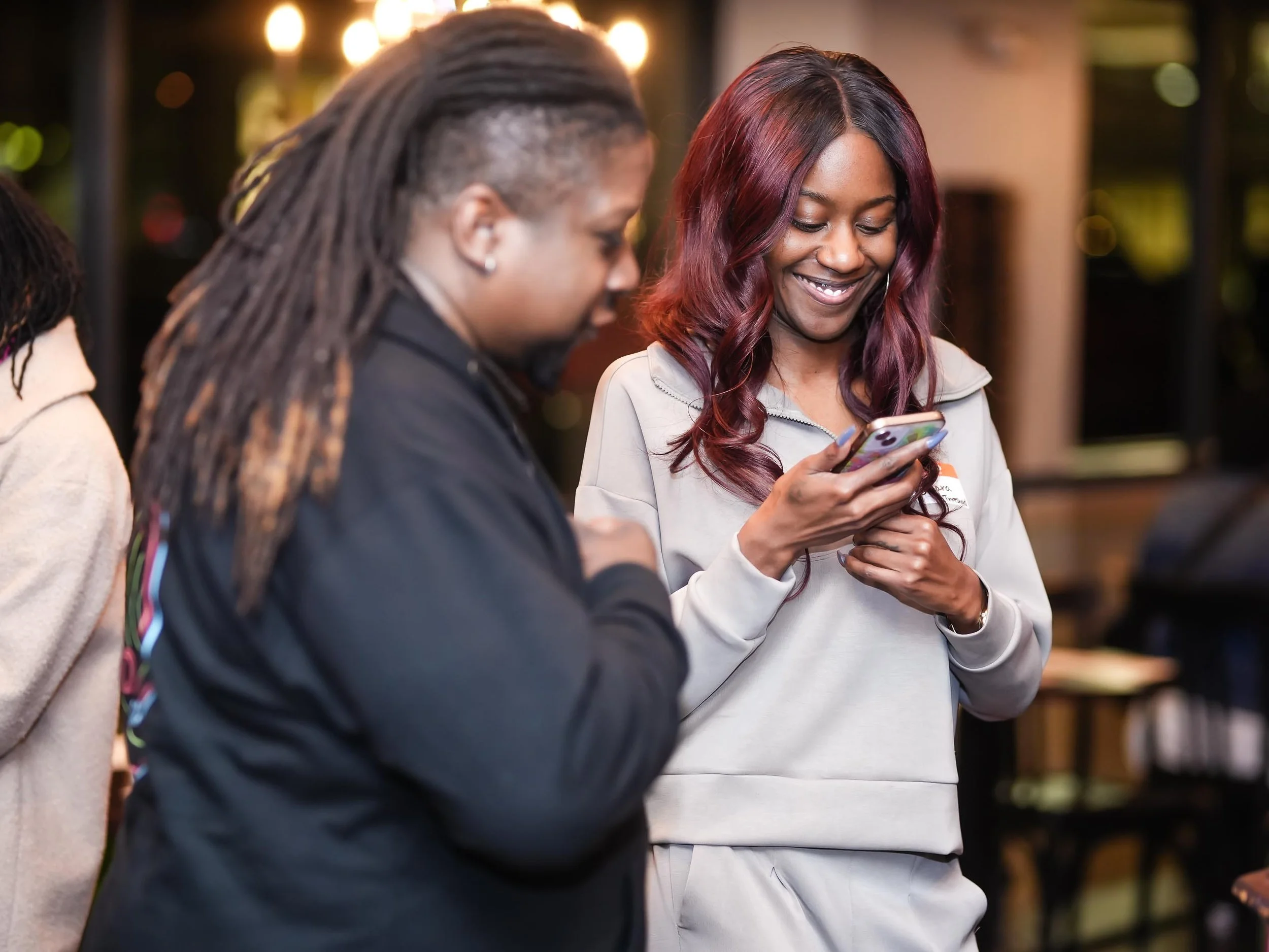 Two women are standing together, smiling and looking at a smartphone at Threshold Social Event