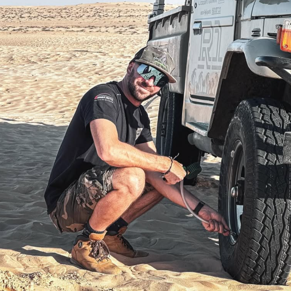 Uomo che aggiusta la ruota di un veicolo fuoristrada in un deserto.