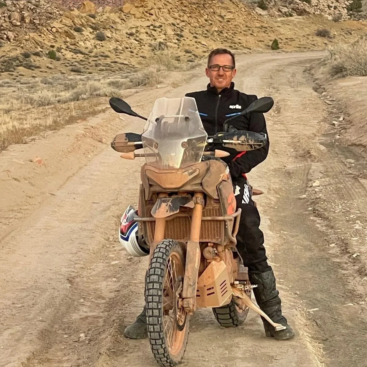 Uomo appoggiato a moto da avventura sulla strada sterrata in ambiente desertico.