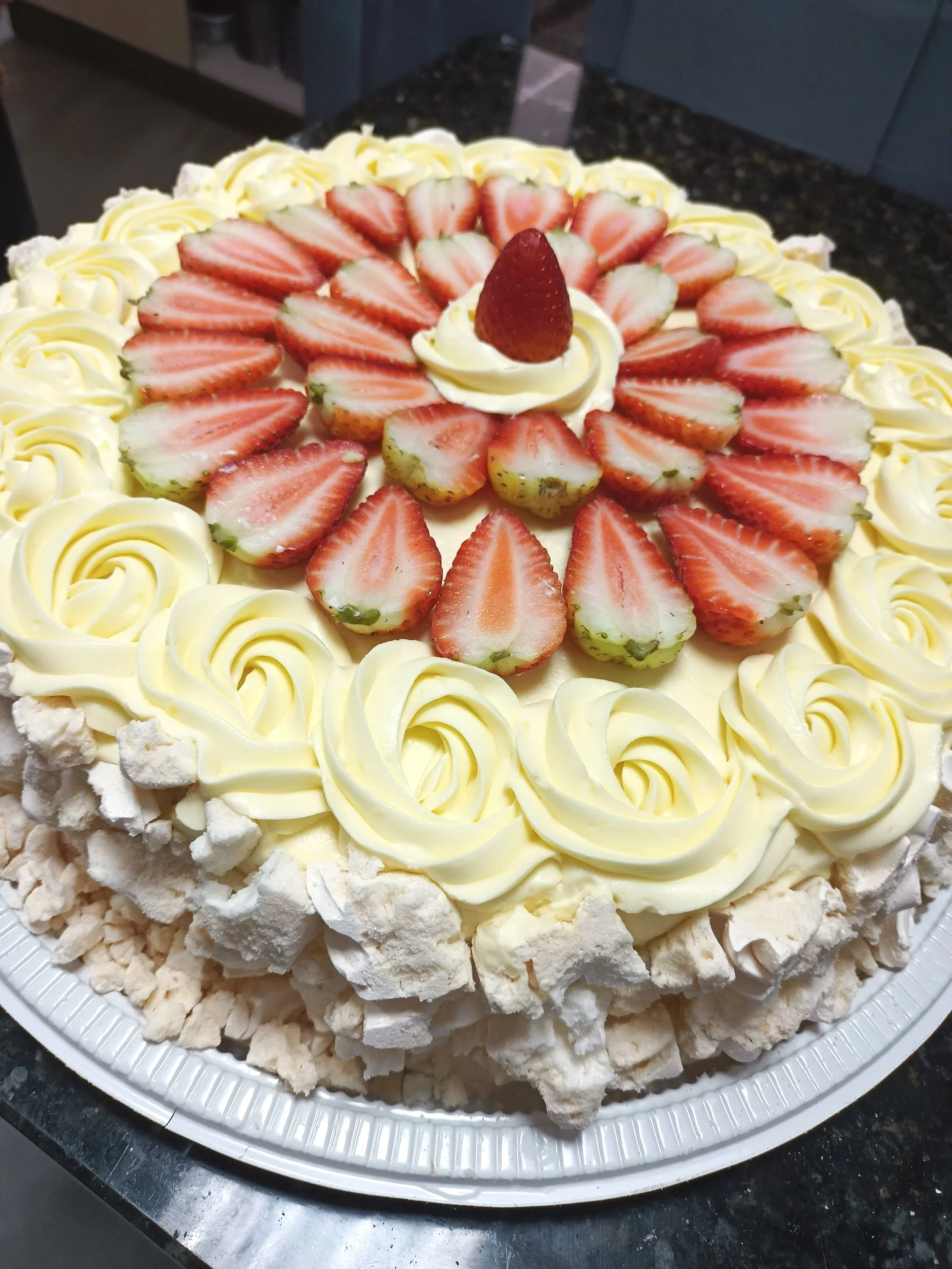 Bolo decorado com morangos fatiados, chantilly e rosetas de creme, com cobertura de pedaços de merengue ou suspiro na borda