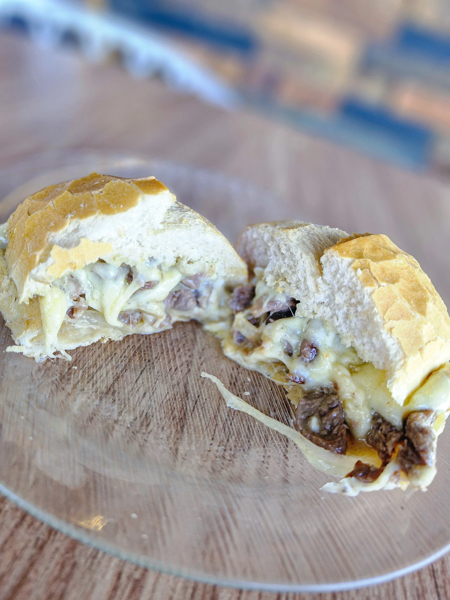 Porção de pão recheado com queijo e carne, parcialmente aberta, colocada sobre um prato de vidro na mesa.