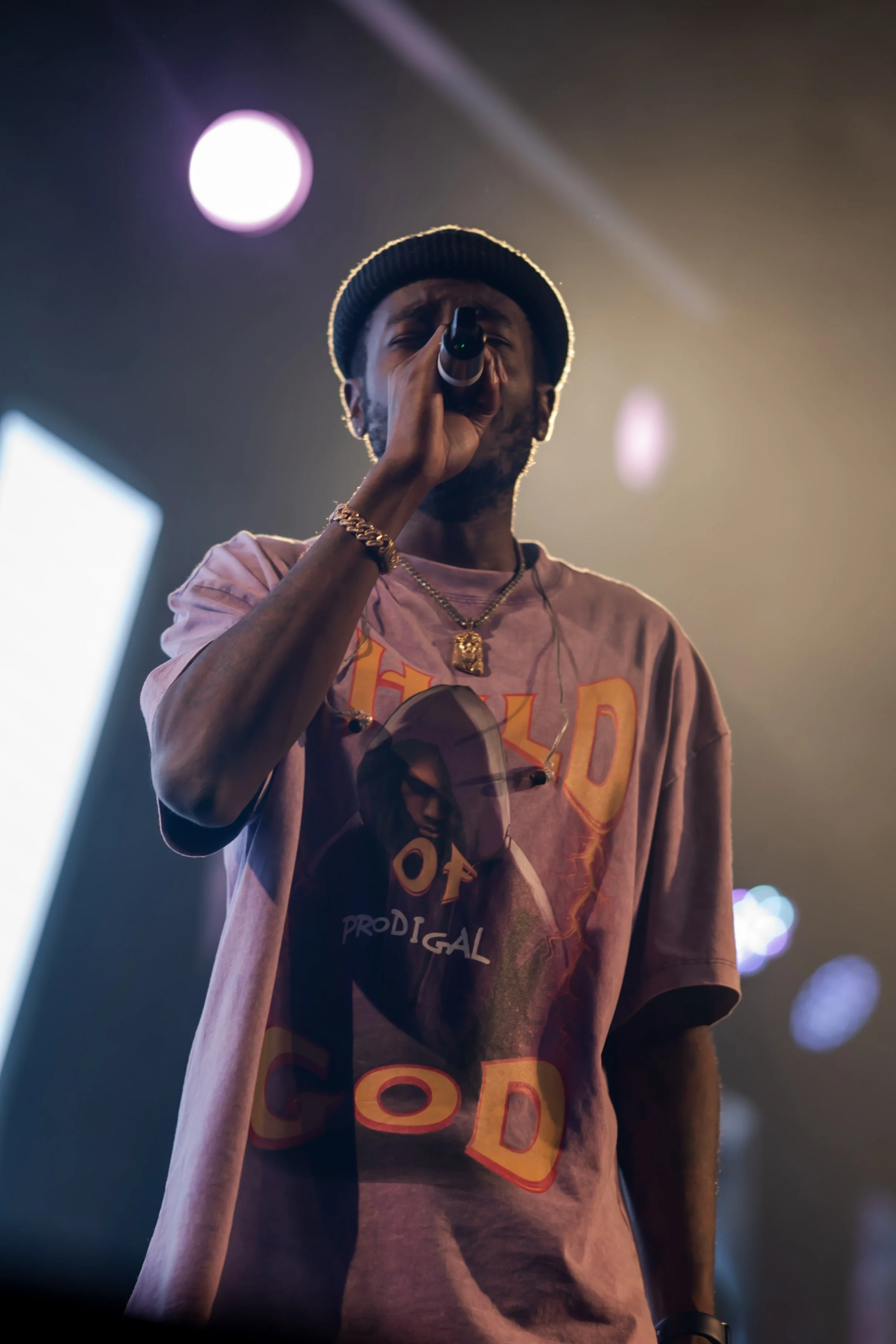 A man singing into a microphone during a live performance under colorful stage lights.
