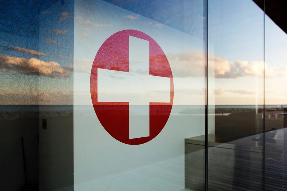 Reflection of a sunset sky with clouds on glass window featuring a red cross symbol.