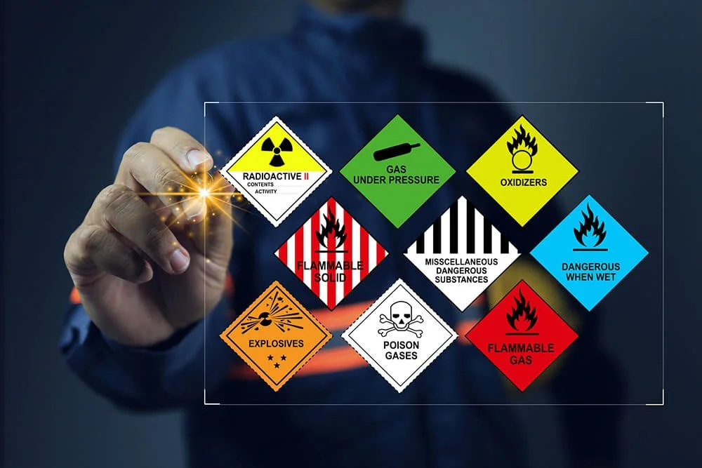 A person in a blue shirt drawing safety hazard symbols for chemicals and materials on a digital screen, including radioactive, gas under pressure, oxidizers, flammable solid, dangerous when wet, explosives, poison gases, and flammable gas.