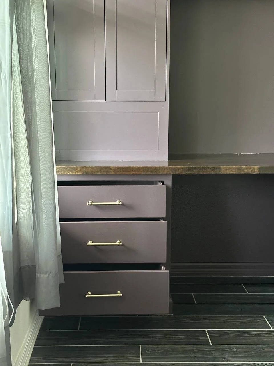 Three partially open desk drawers with metallic pulls beneath a wood worktop and tall painted cabinet.
