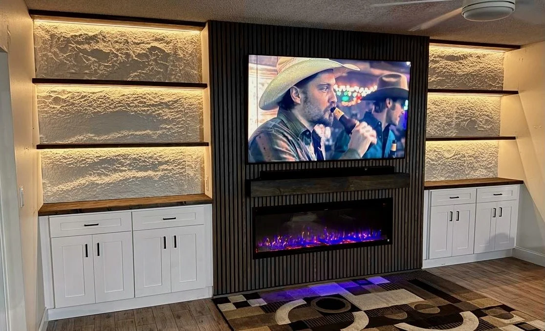Tampa fireplace media wall with dark vertical slats, white storage cabinets, wood shelves, and warmly lit textured niches.