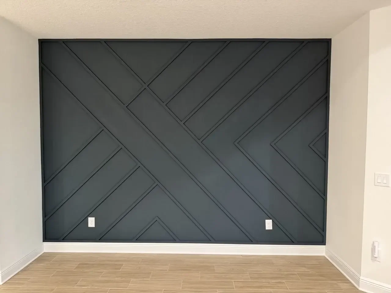 Charcoal geometric board-and-batten accent wall in Bradenton with diagonal trim, a perimeter frame, and contrasting white baseboards.
