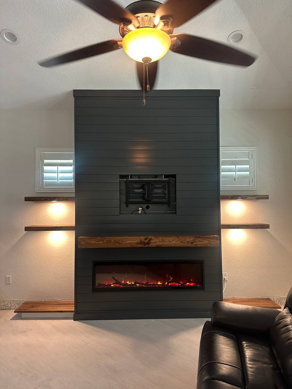 Dark shiplap fireplace wall in Orlando with a wood mantel, illuminated floating shelves, and a TV mounting bracket.