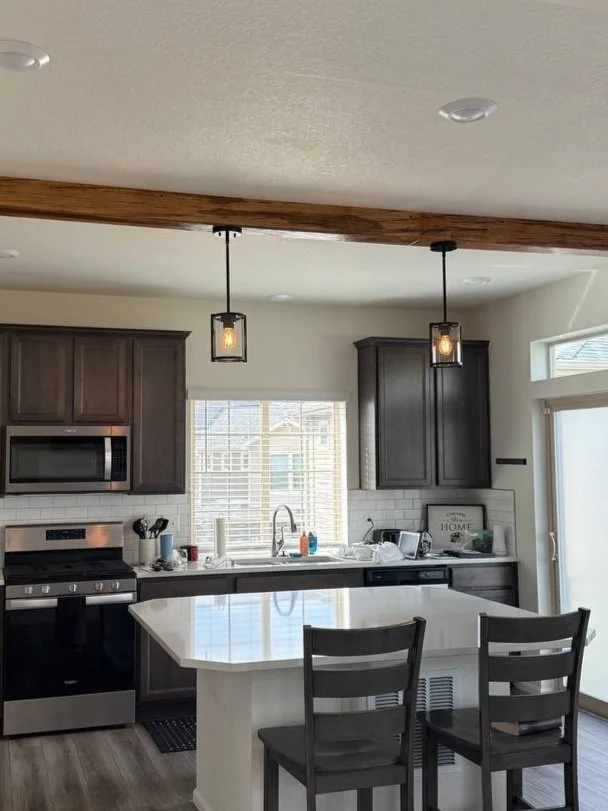 Modern kitchen with dark wood cabinets, stainless steel appliances, a white island, and pendant lights