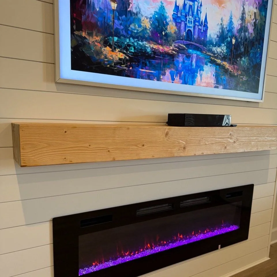 Flat-screen TV showing a colorful impressionistic castle scene, mounted above a wooden mantel shelf with a black soundbar, and beneath an electronic fireplace with purple and orange flames.