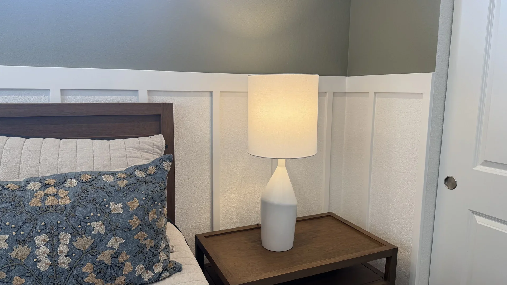White board-and-batten trim and pistachio walls beside a wooden bed and bedside lamp in a Los Angeles bedroom.
