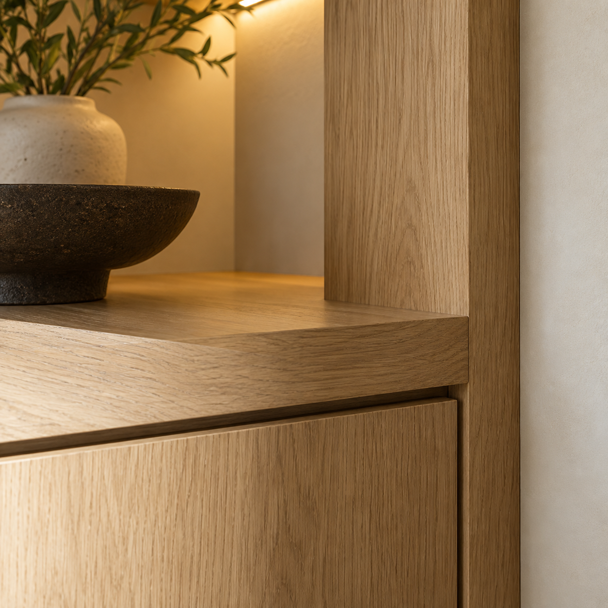 Close-up of a wooden cabinet with decorative bowls and a plant in a beige vase on top.