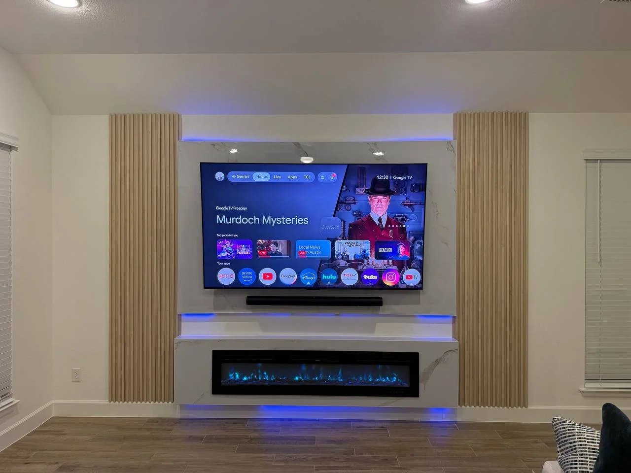 Houston media wall with wood slat panels, a marble-look TV surround, blue LED lighting, and a linear electric fireplace.