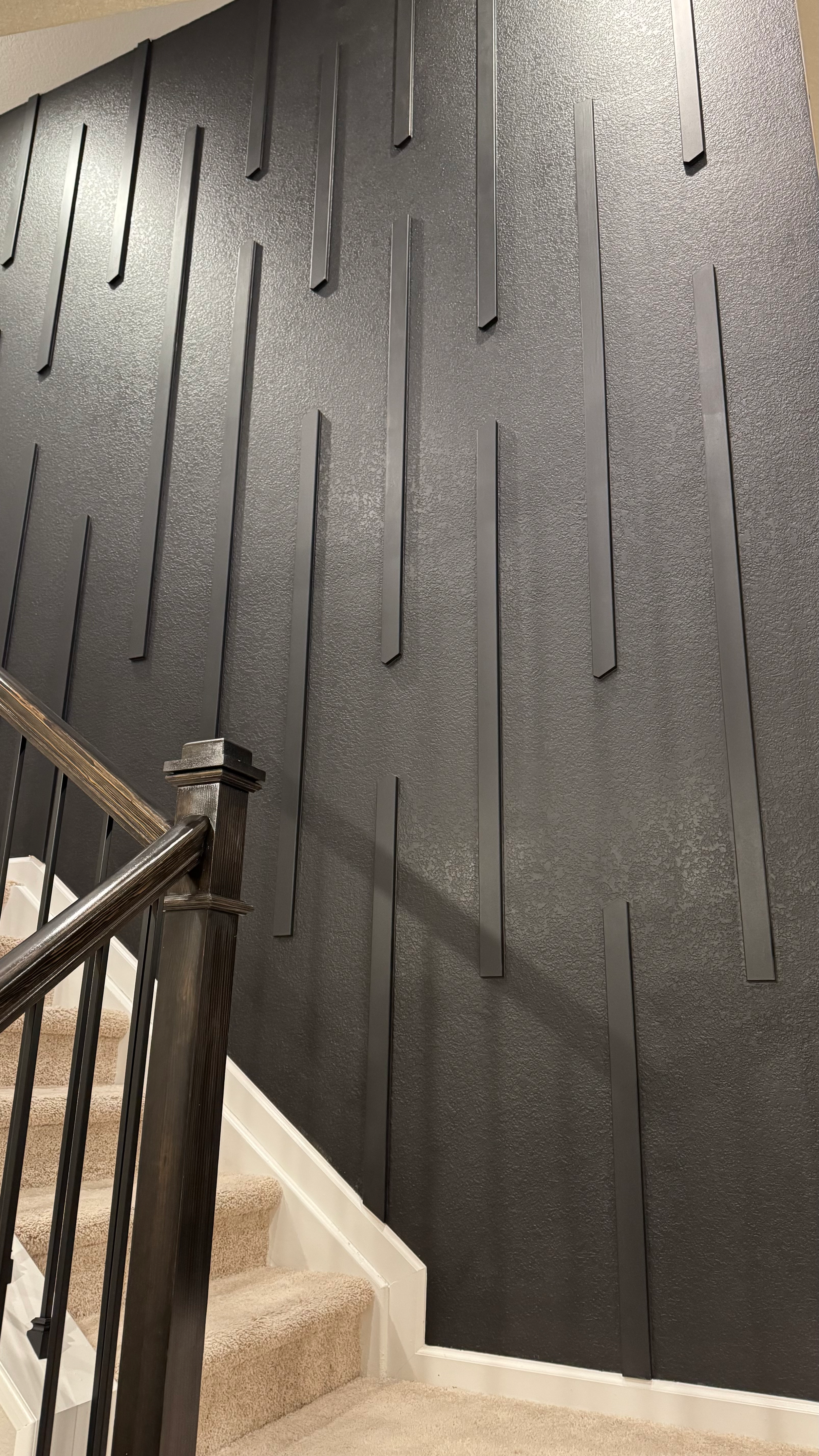 Description: close-up of matte black accent wall with vertical trim elements and staircase railing