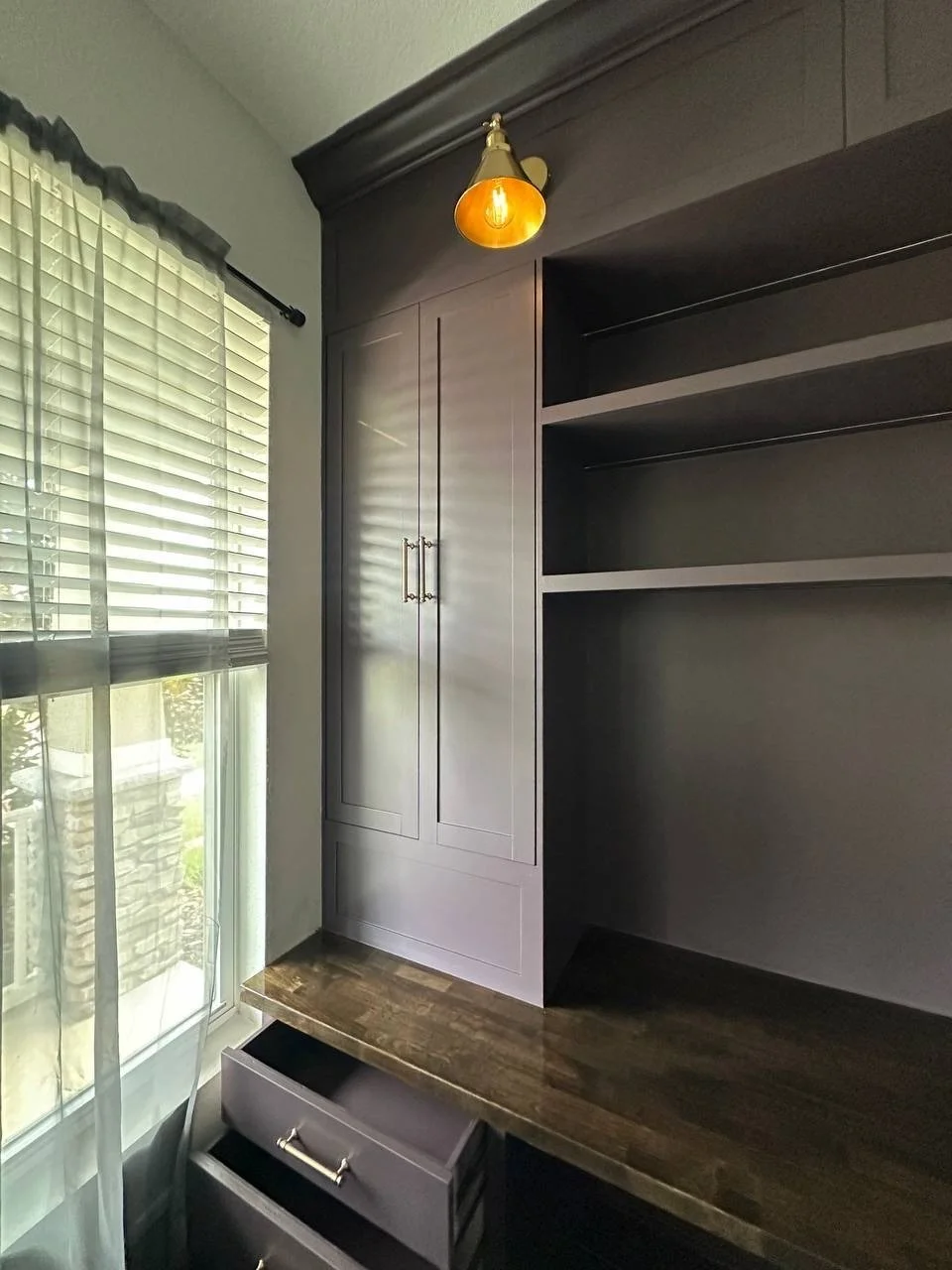 Office cabinet and open shelves beside a window, with a wood desktop, brass-toned sconce, and partially open drawers.