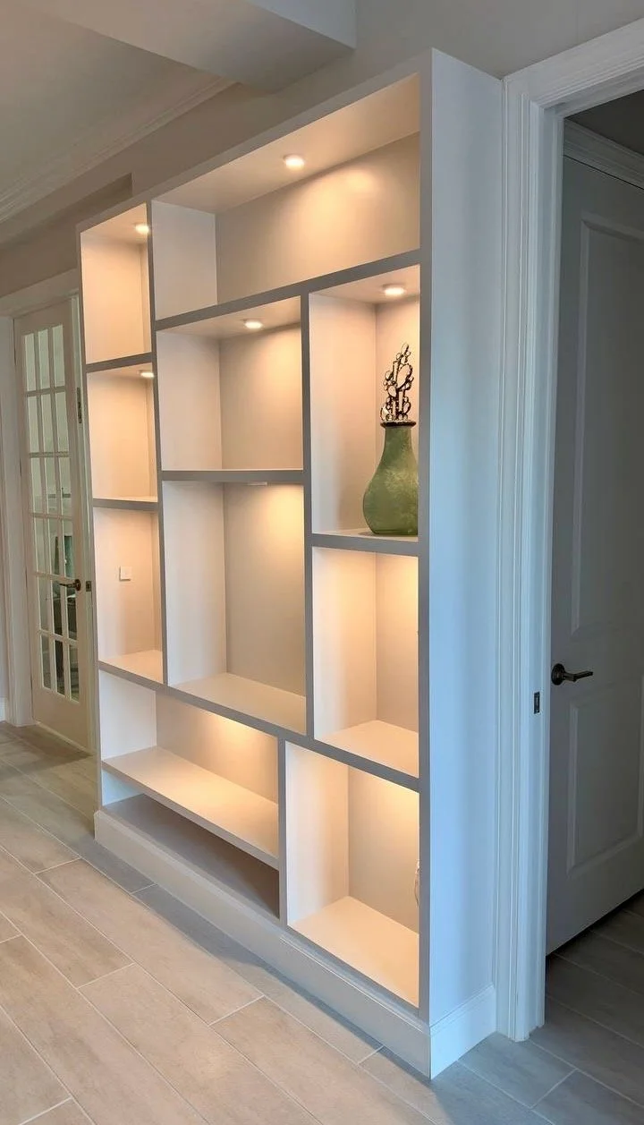 White built-in display shelves with warm recessed lighting and a green vase beside a doorway.