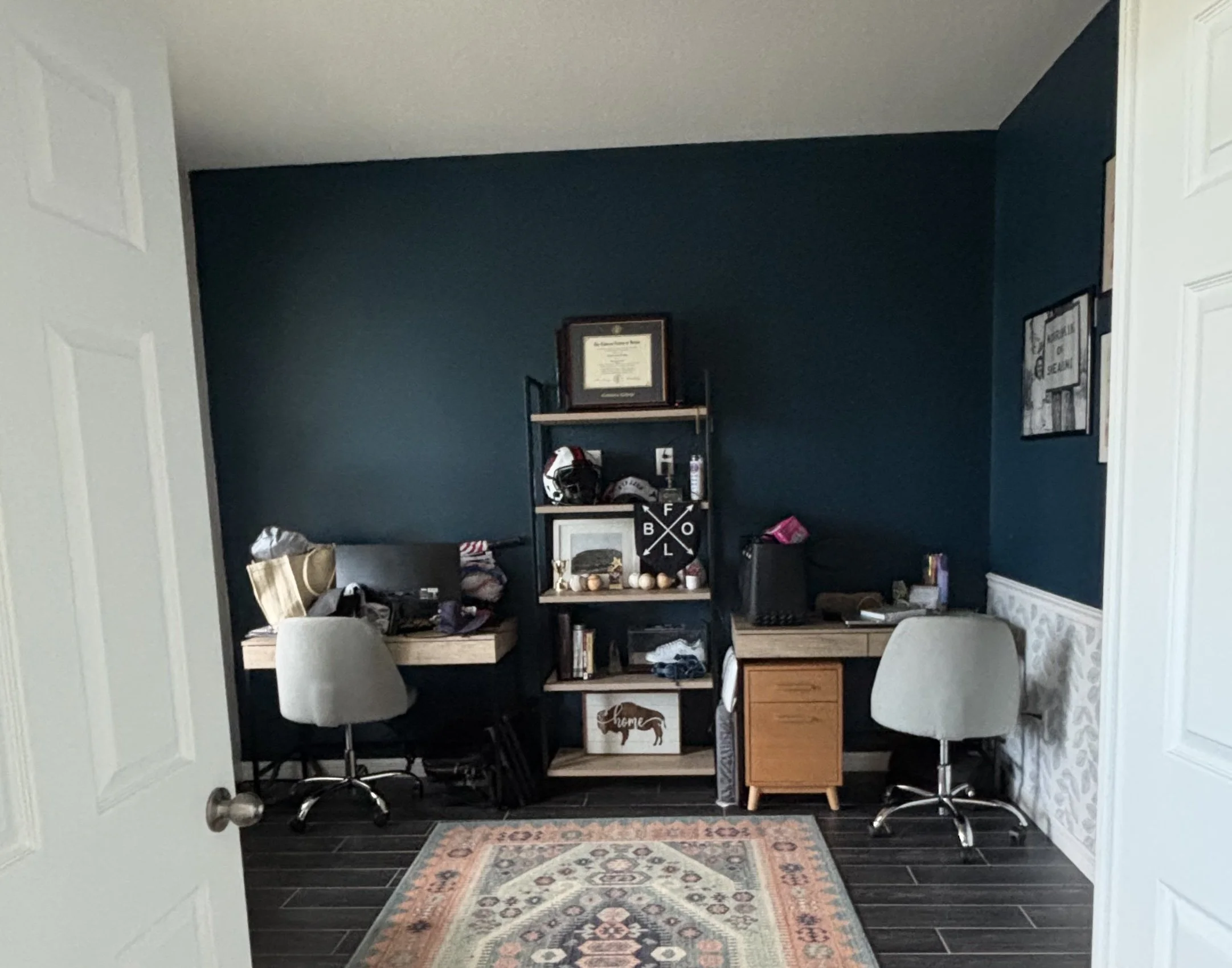 Orlando home office before renovation, with two separate desks and a freestanding shelving unit against a dark teal wall.