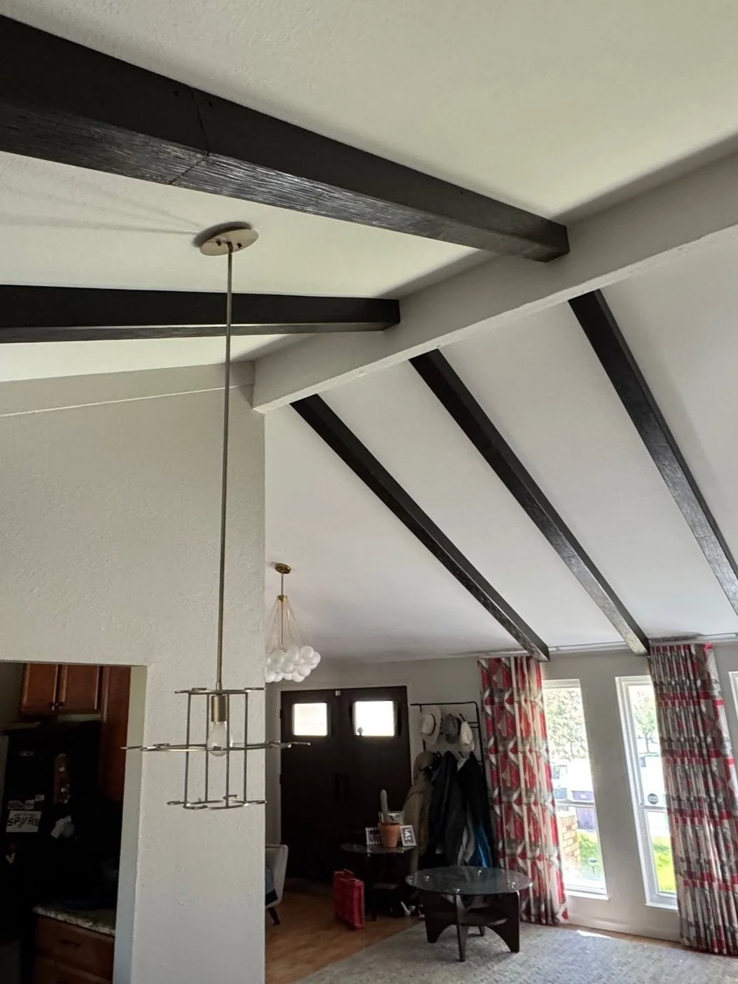 Living room with white ceiling, dark wood beams, and large windows with red and white patterned curtains.