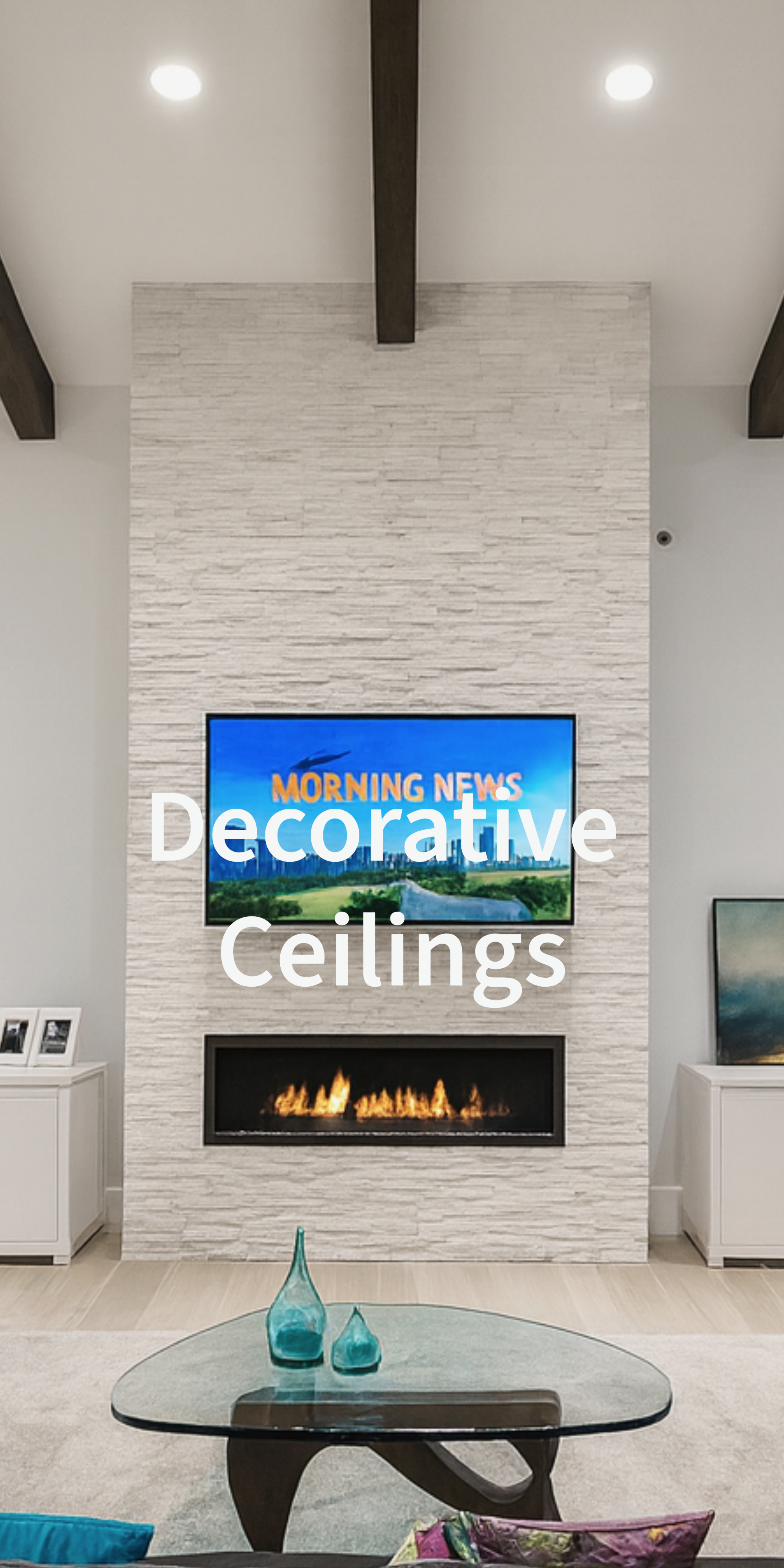 Decorative ceiling with wood beams and recessed lighting above a modern living room with a fireplace, television, and glass table.