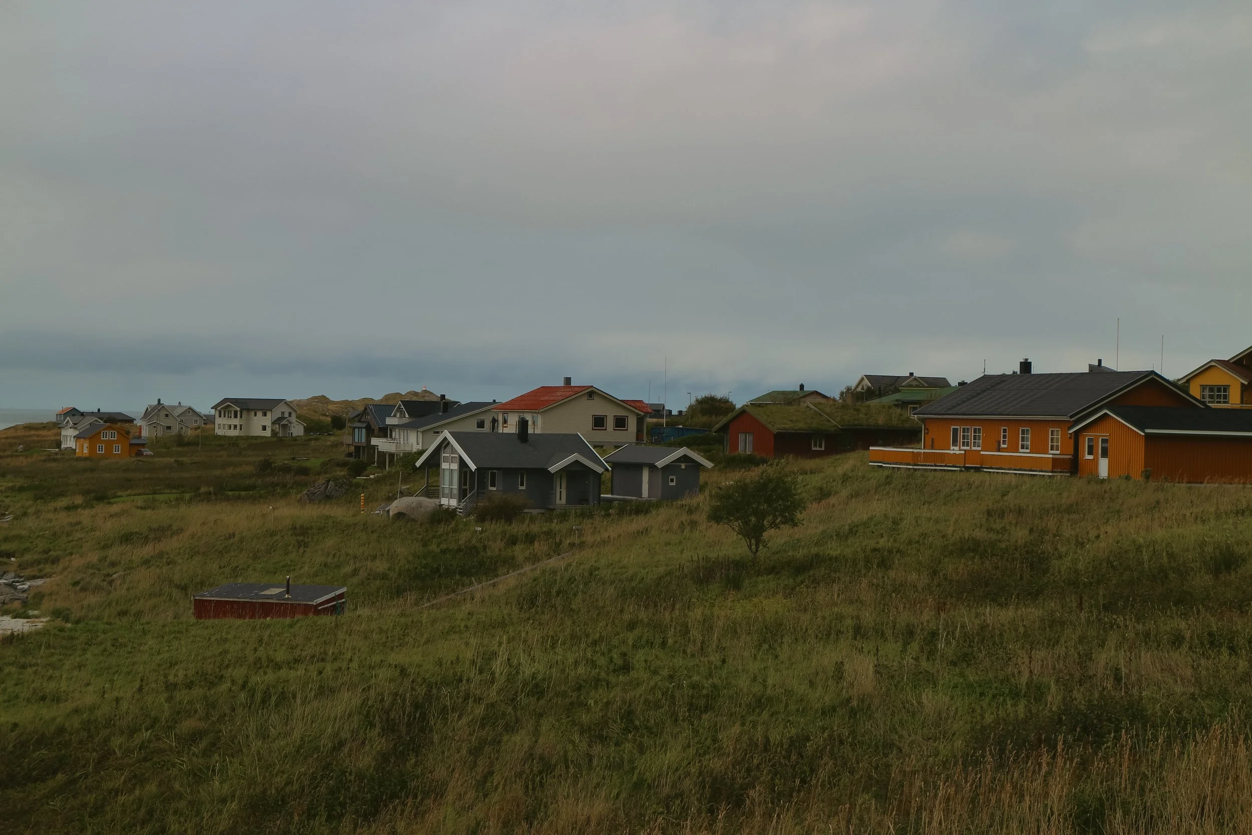 Hillside community with colorful houses, grassy terrain, and cloudy sky.