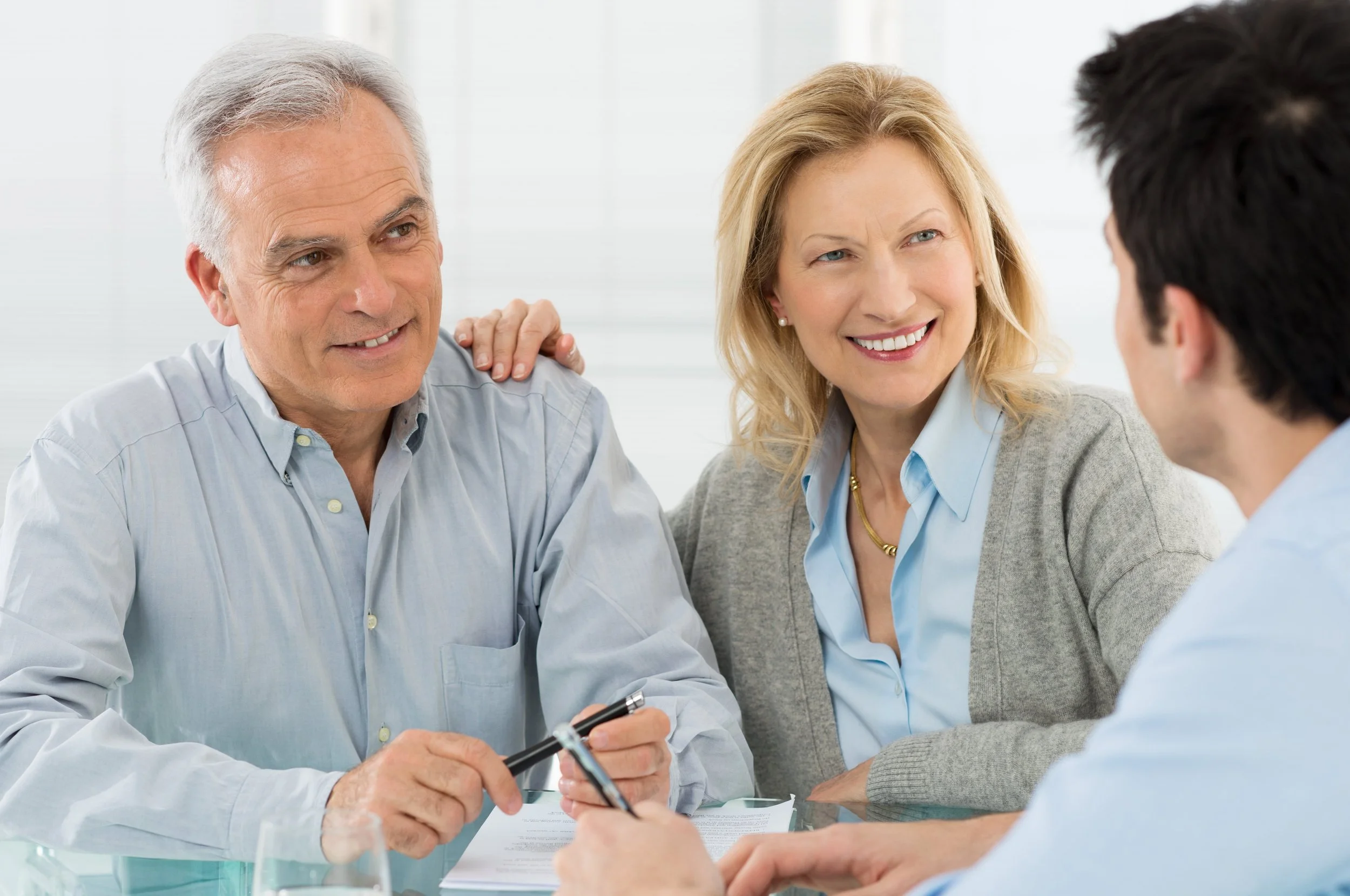 Older man and woman talking with younger man at a meeting table, smiling and engaging in conversation.