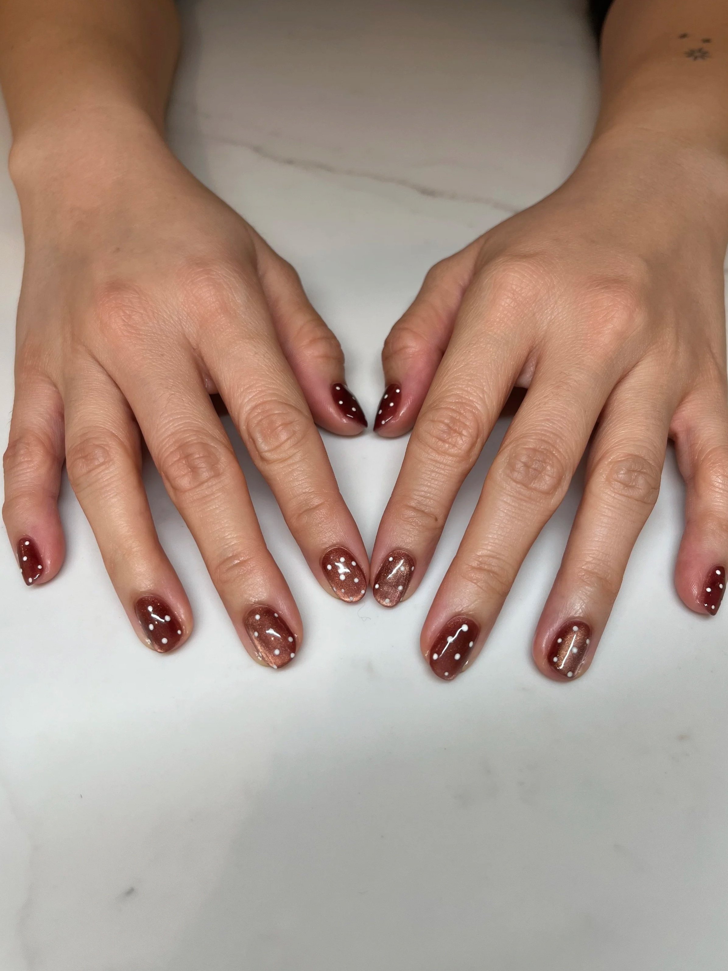 Gel manicure with a burgundy cat eye and white polka dots 