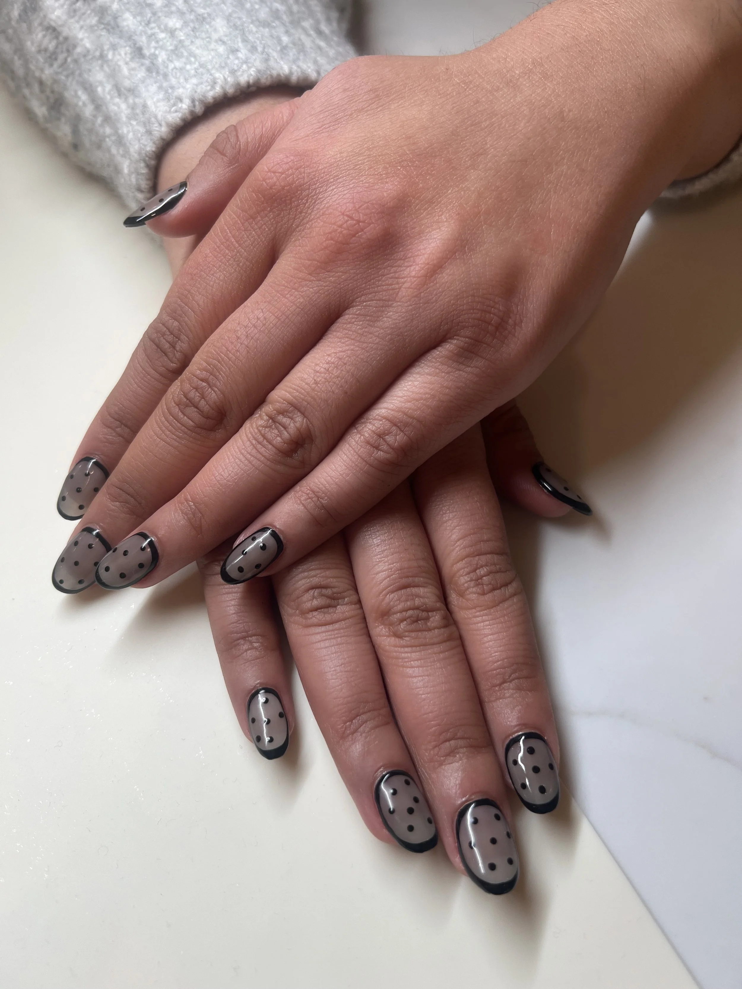 Gel extensions with a sheer black base, black polka dots, and a black border