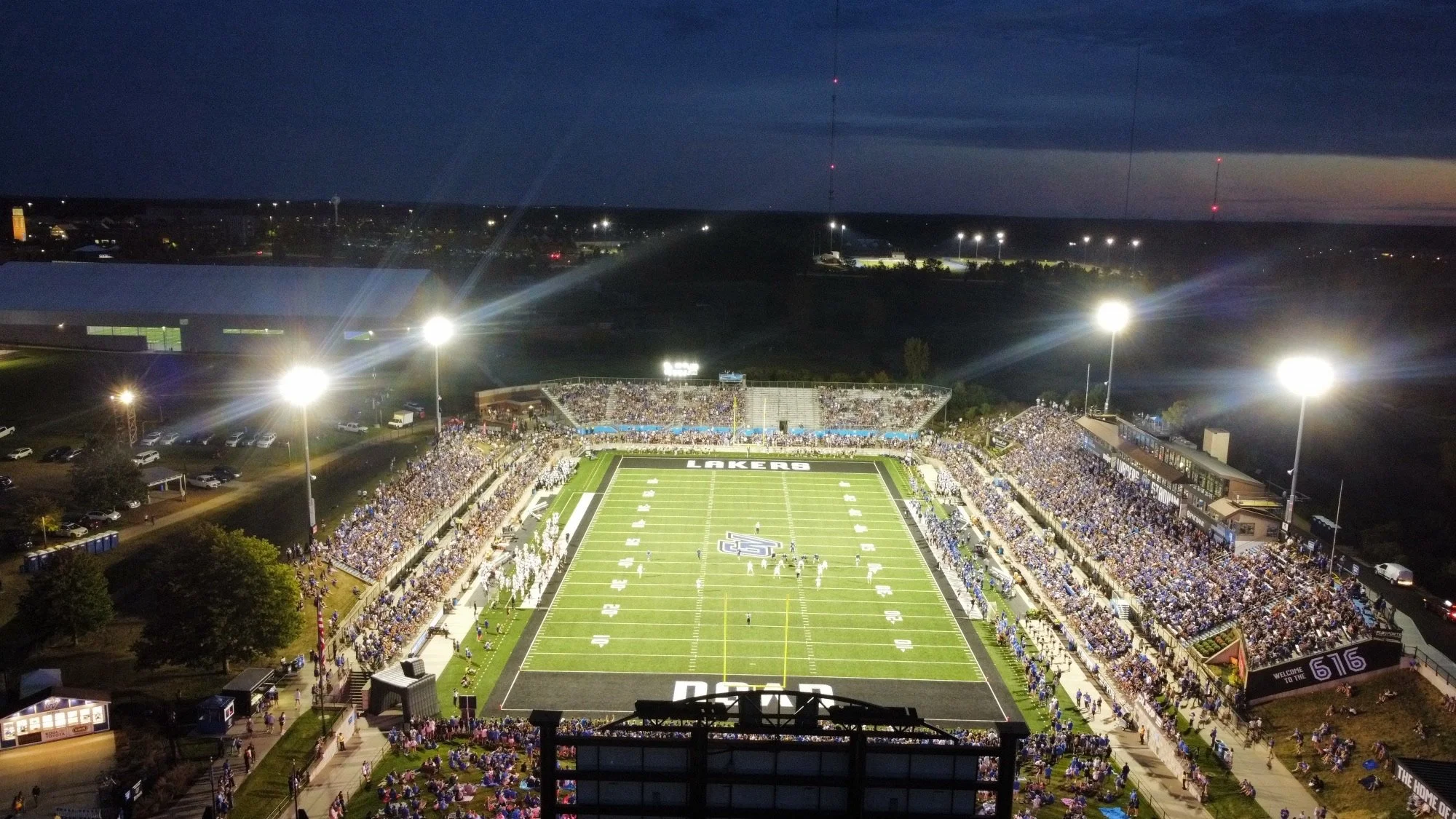 A stadium at night filled with spectators, with bright floodlights illuminating the football field and surrounding seating areas.