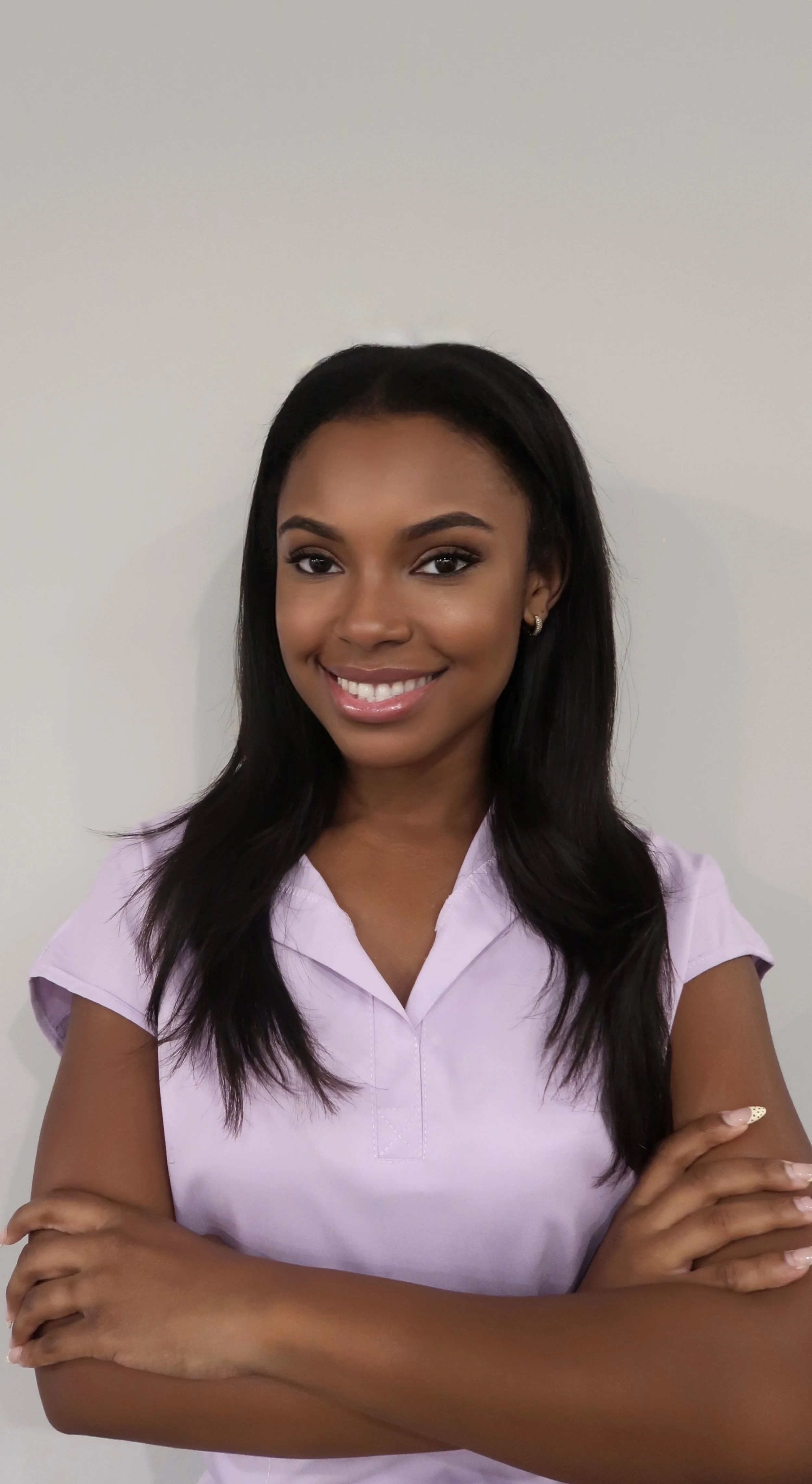 Woman standing against a plain background with her arms crossed in a purple top