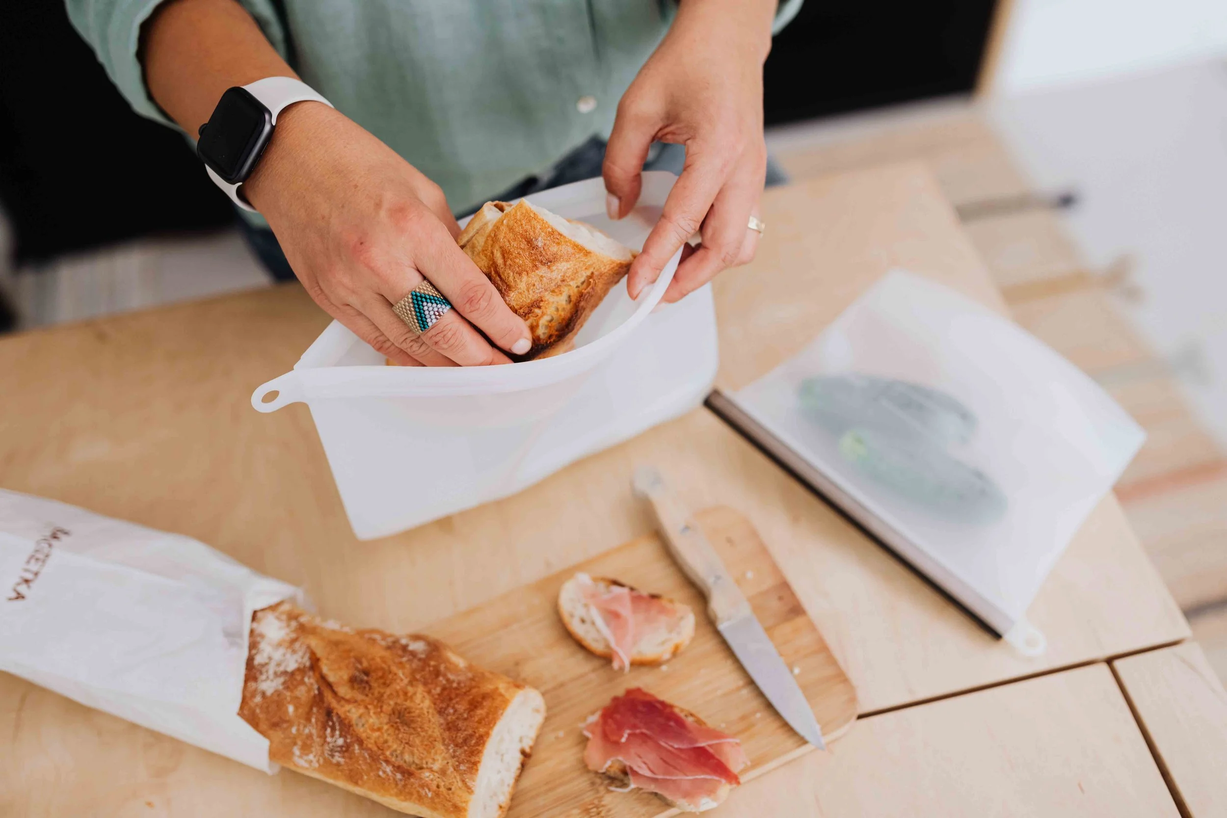 Person preparing a sandwich with toasted bread and sliced cured meat on a wooden cutting board.