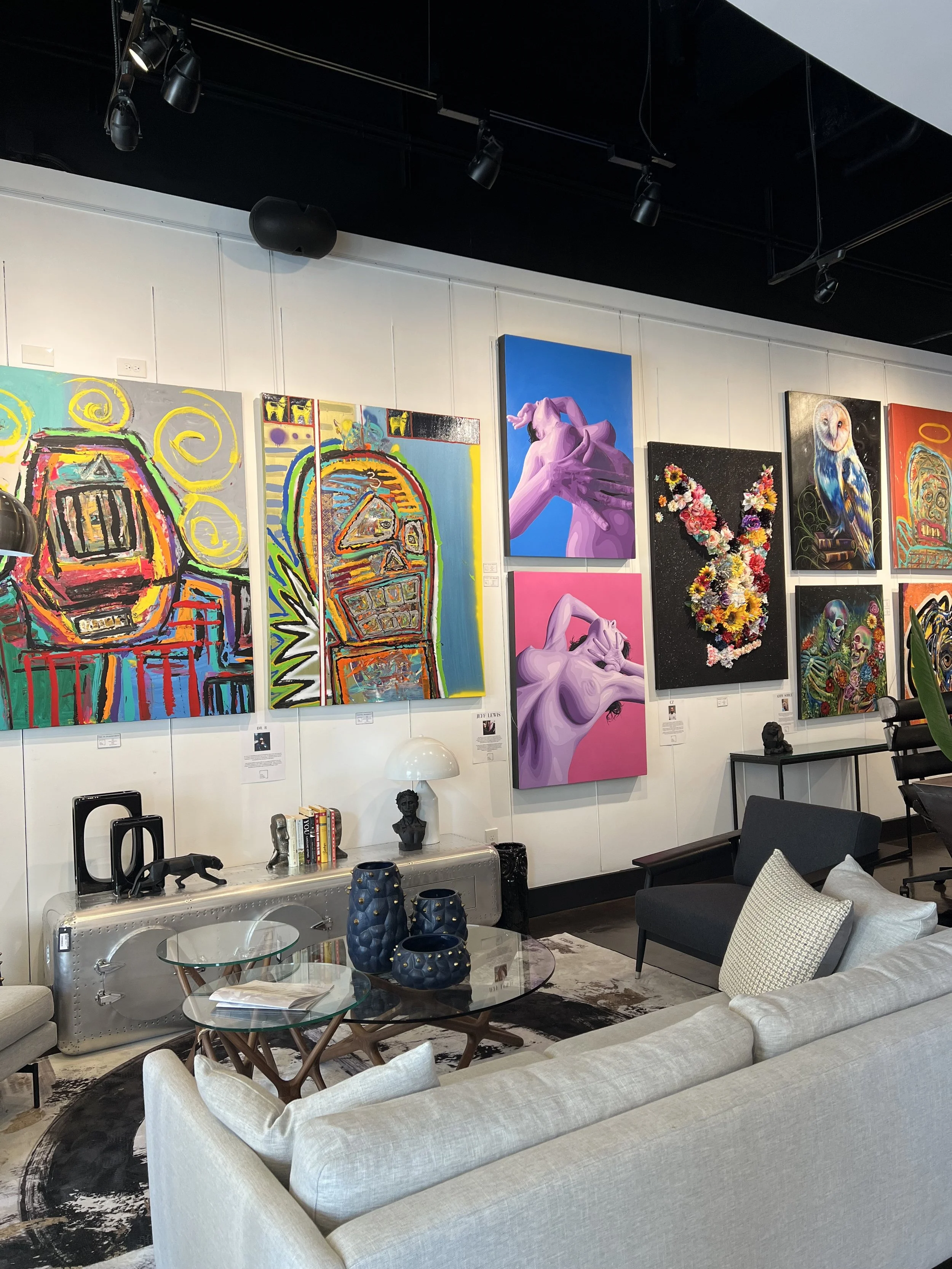 A living room with white sofa, patterned rug, glass coffee table, black armchair, decorative blue vases, artwork on the wall, and a modern aesthetic.