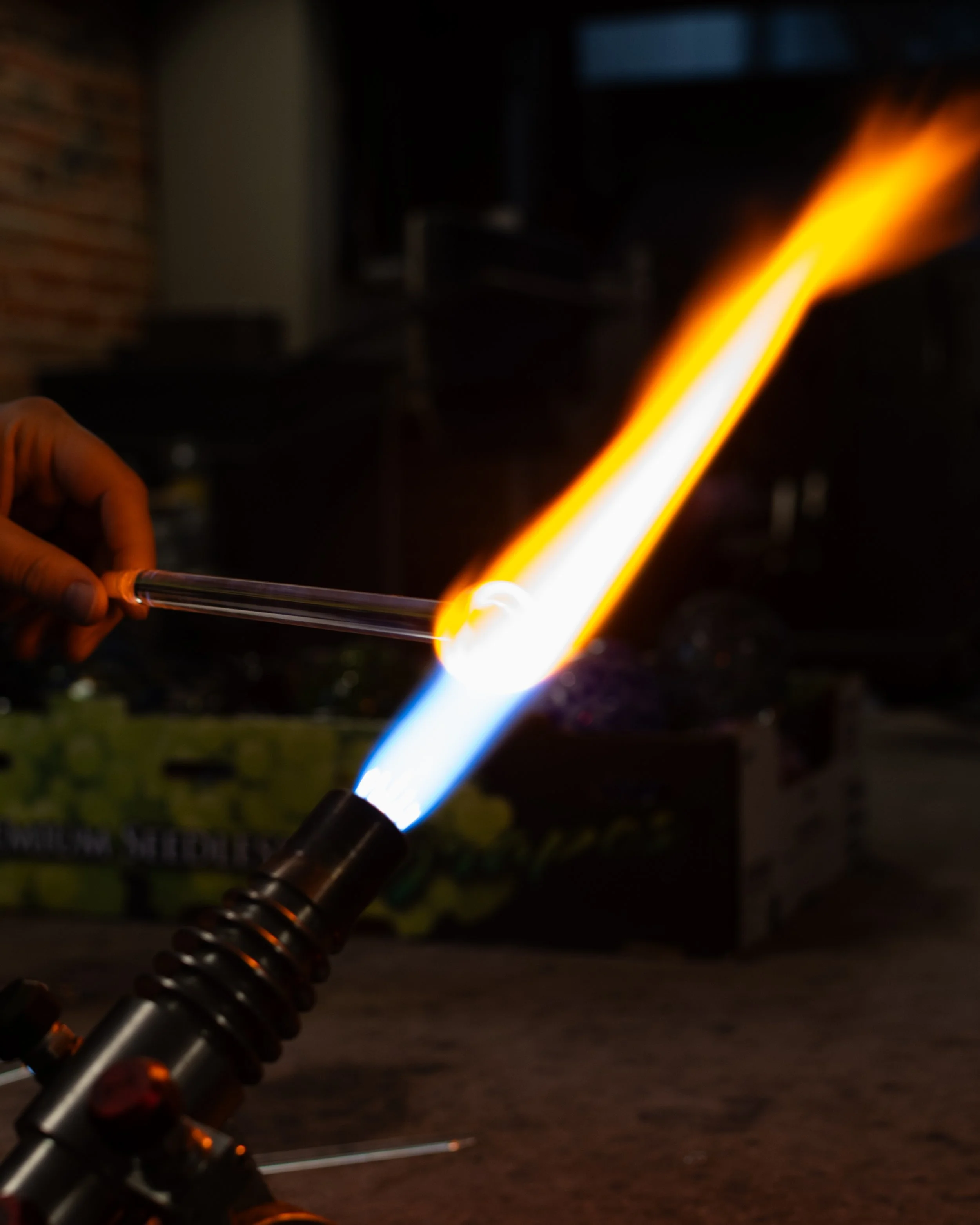 A person holding a blowtorch with a bright flame, used for shaping or heating glass.